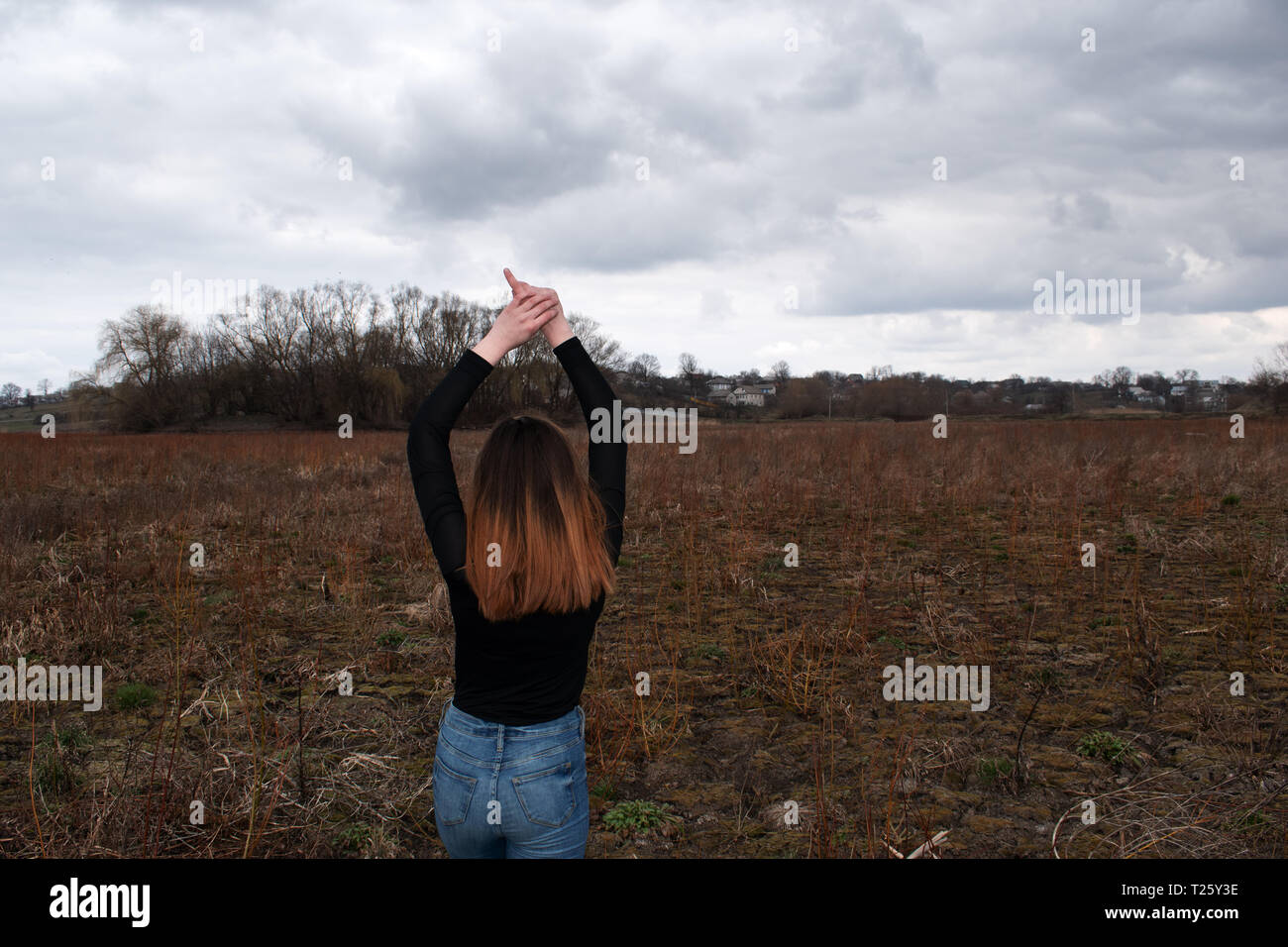 The girl is back in a black sweater. under the overcast sky. Hands up Stock Photo