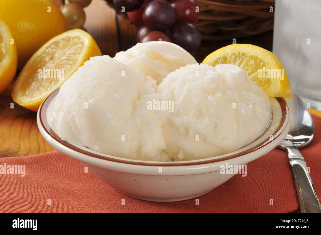 A bowl of lemon sherbet or gelato near a basket of grapes Stock Photo