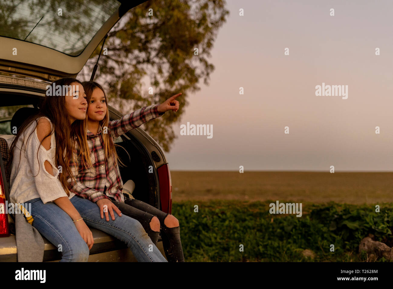 Two sisters sitting at opened tail watching sunset together Stock Photo