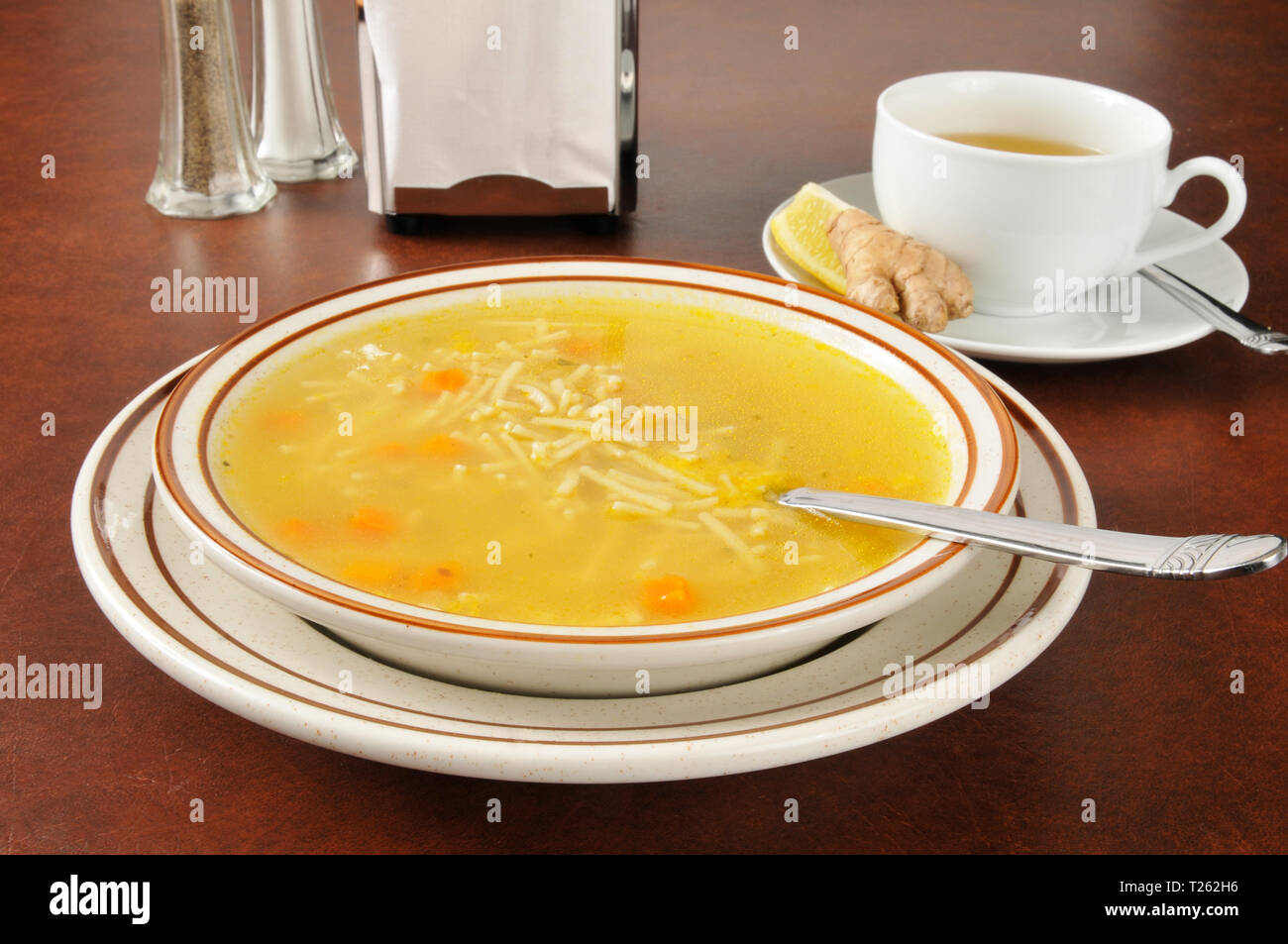 A bowl of hot chicken noodle soup with green tea, lemon and ginger, a