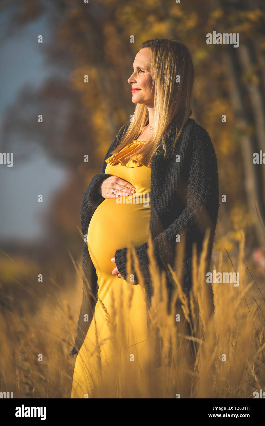 Smiling pregnant woman standing in nature in autumn Stock Photo
