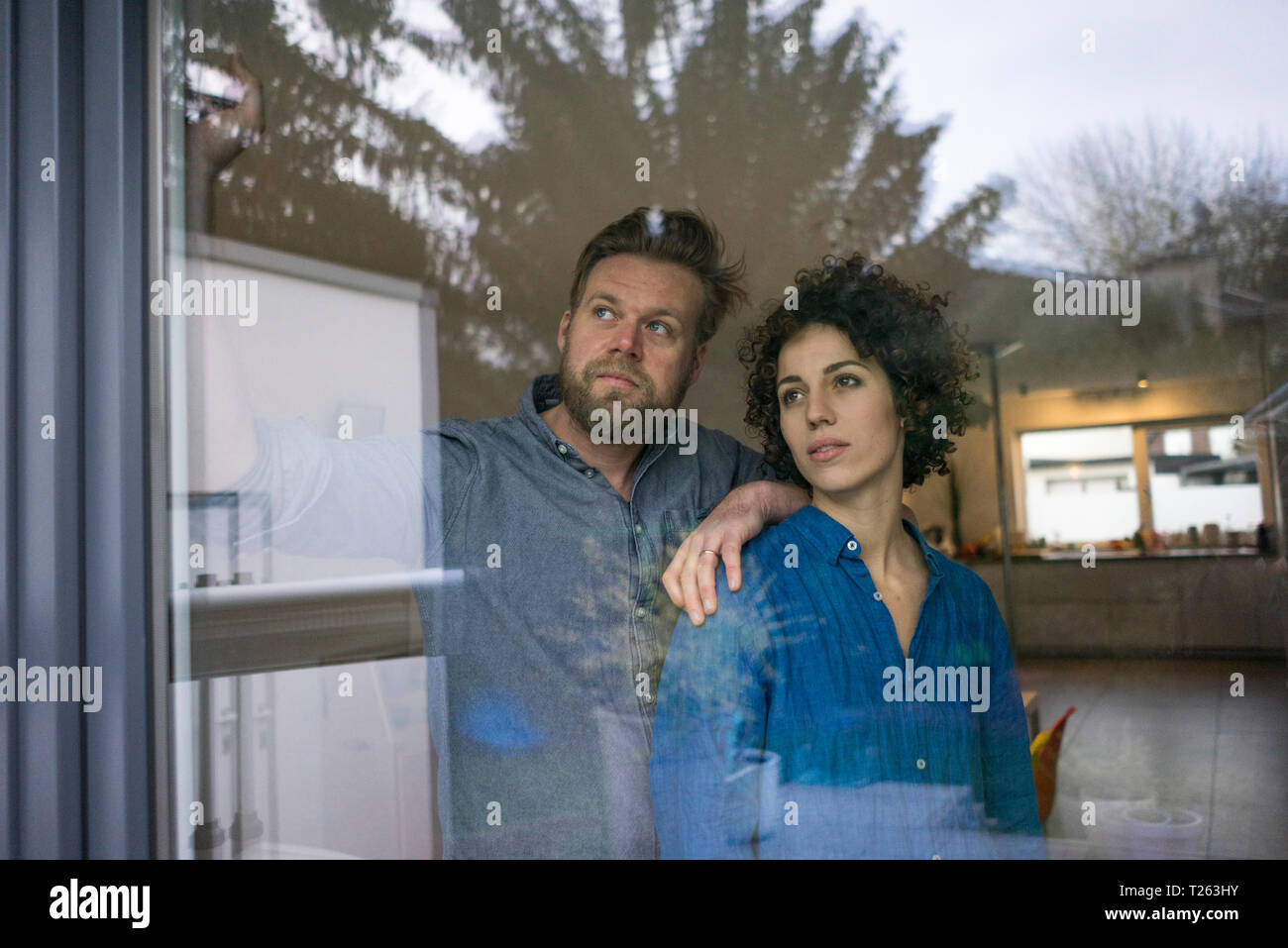 Serious couple behind window at home looking out Stock Photo - Alamy