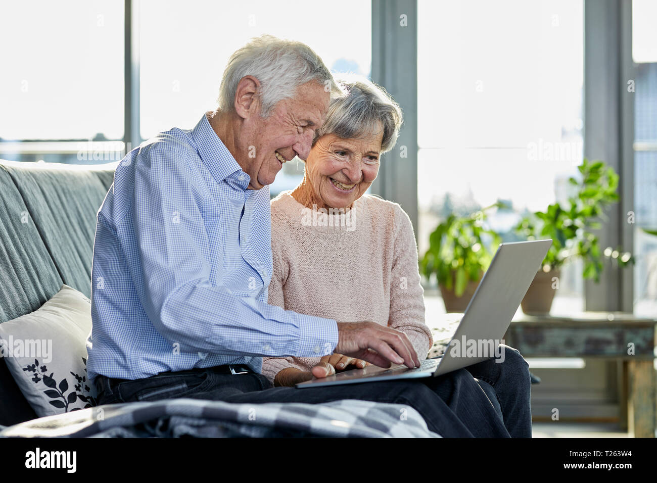 Senior couple sitting together on couch using laptop Stock Photo