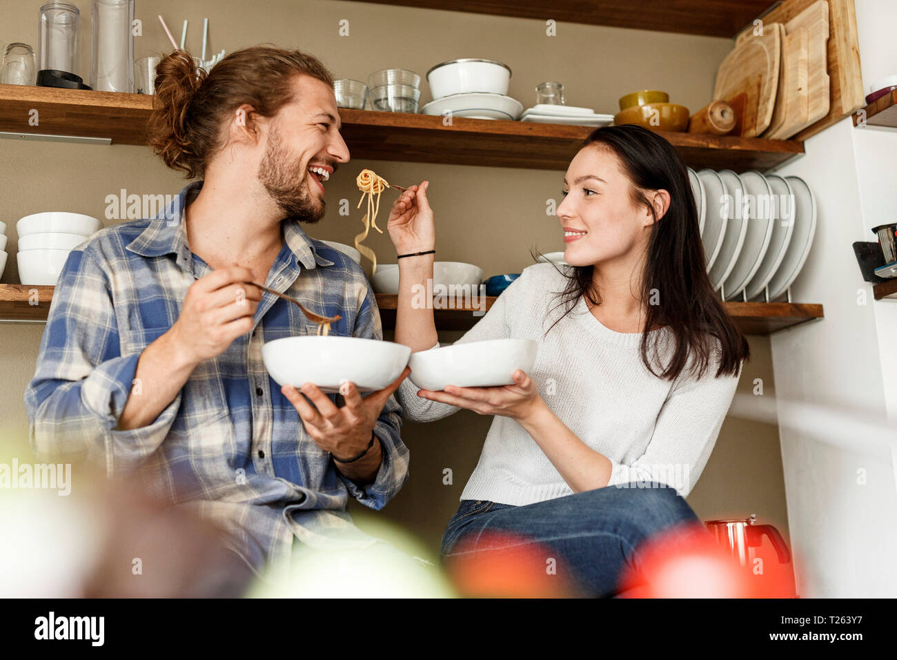 Happy couple sitting in kitchen, eating spaghetti Stock Photo