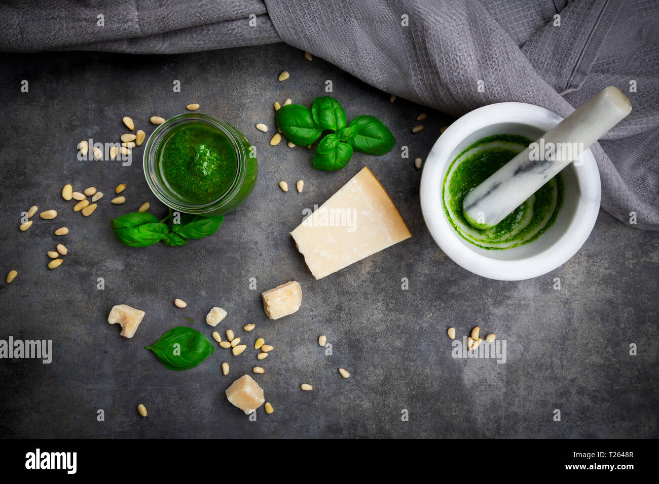 Glass of homemade pesto Genovese, mortar and ingredients on grey ground Stock Photo