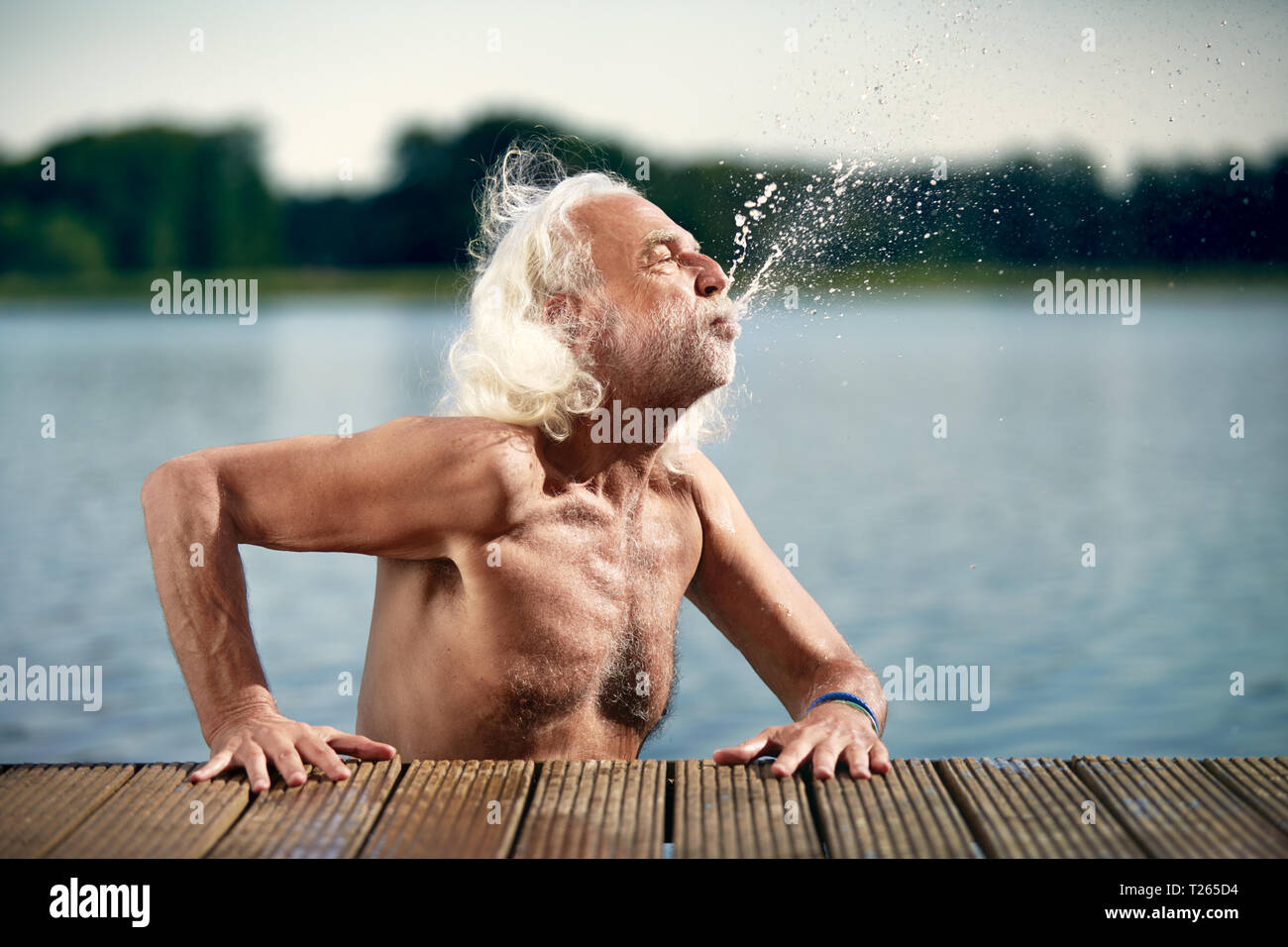 Senior man with white hair leaning on jetty splashing with water Stock Photo