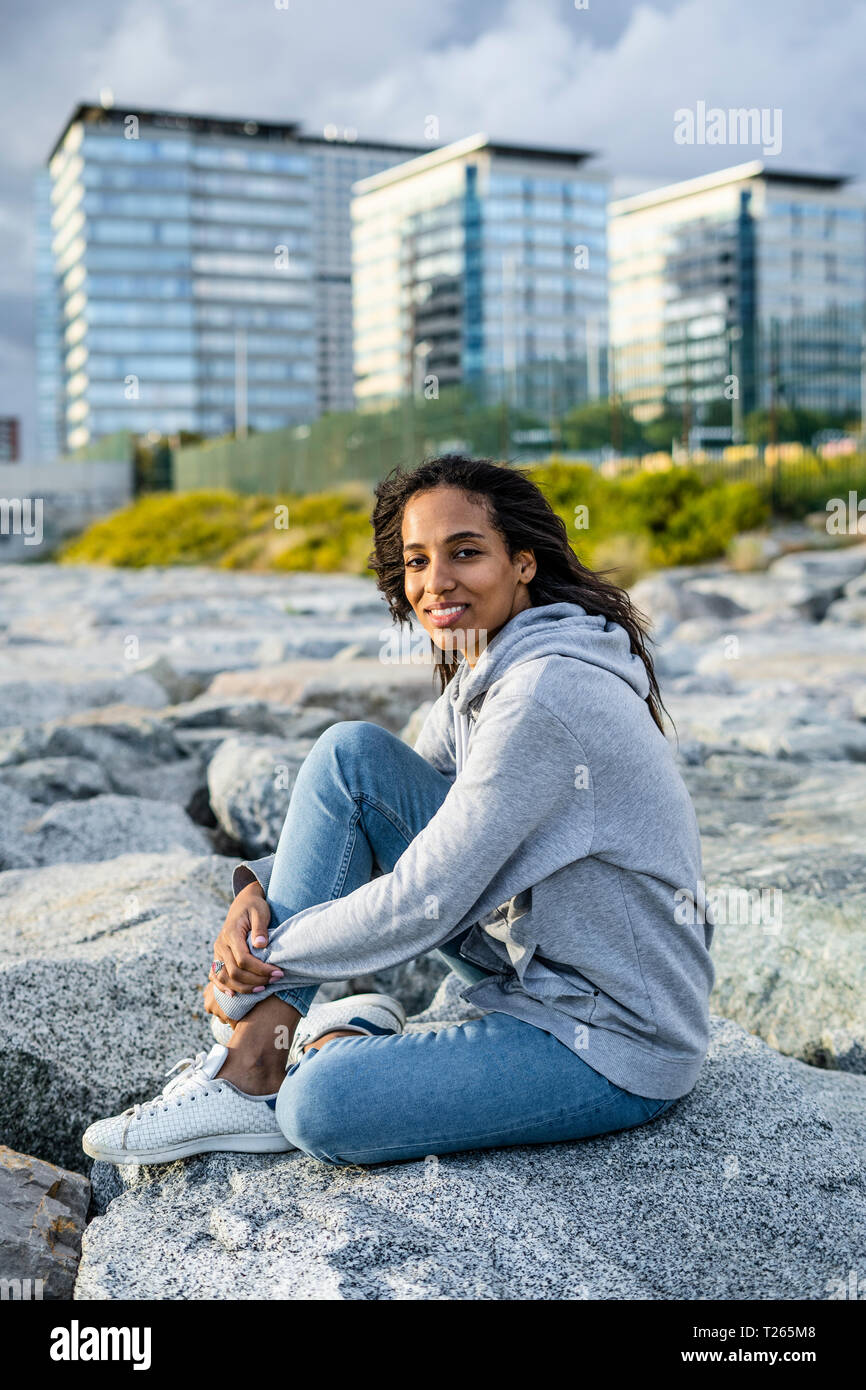 Young woman sitting on rocks at the beach, relaxing Stock Photo - Alamy