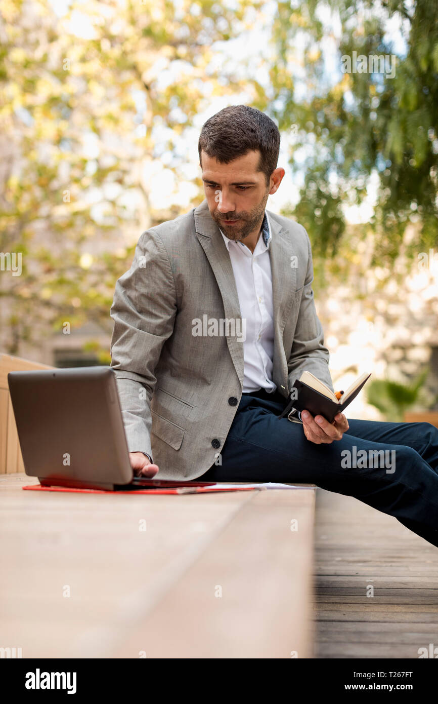 Businessman sitting on a bench using laptop and diary Stock Photo