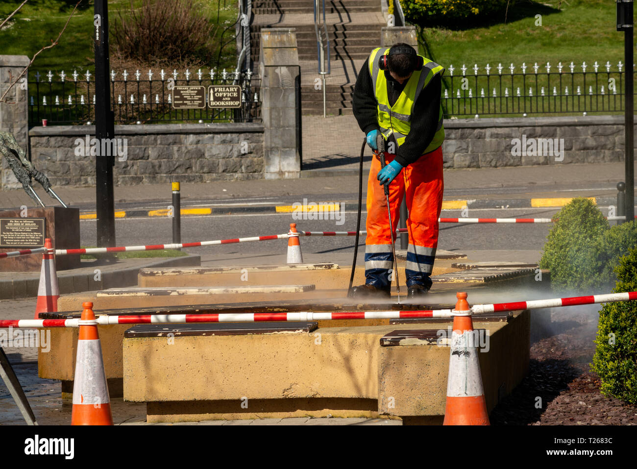 Council worker with pressure washer deep cleaning street benches for springtime cleaning in Killarney, County Kerry, Ireland Stock Photo