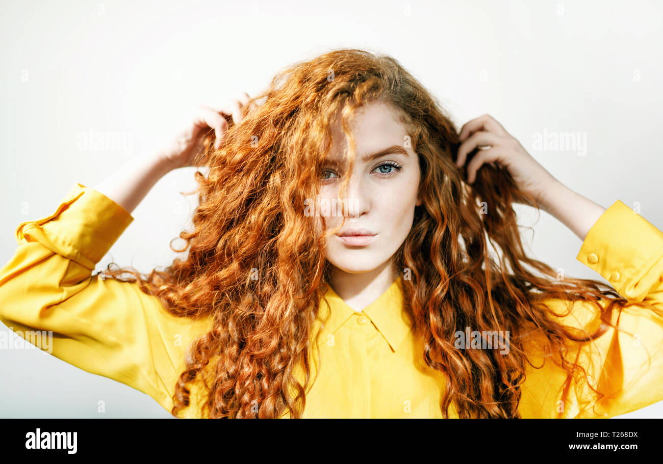 Attractive Ginger Girl Touching Her Curly Hair On The White