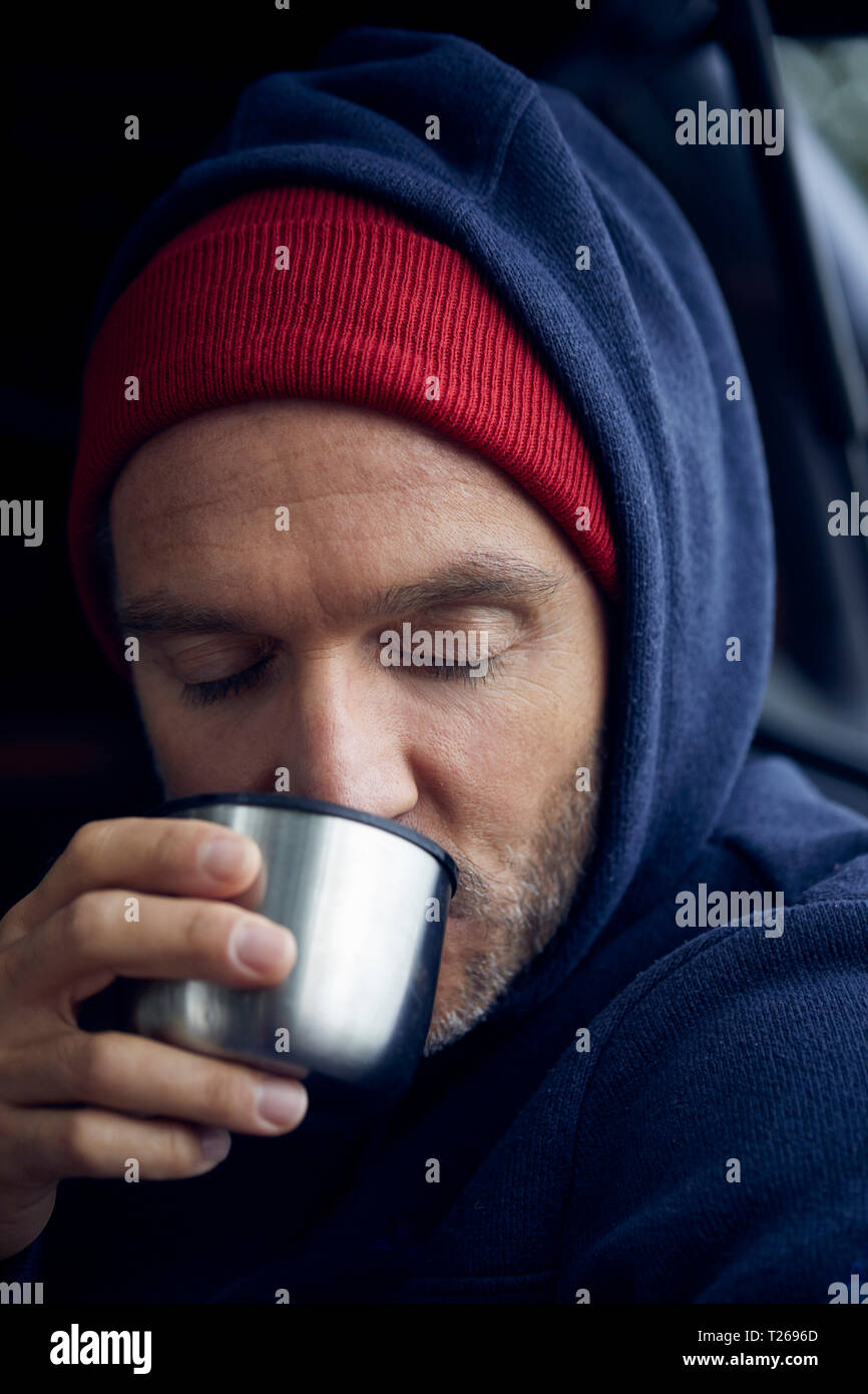 Portrait of mature man wearing red cap and blue hooded jacket drinking Stock Photo