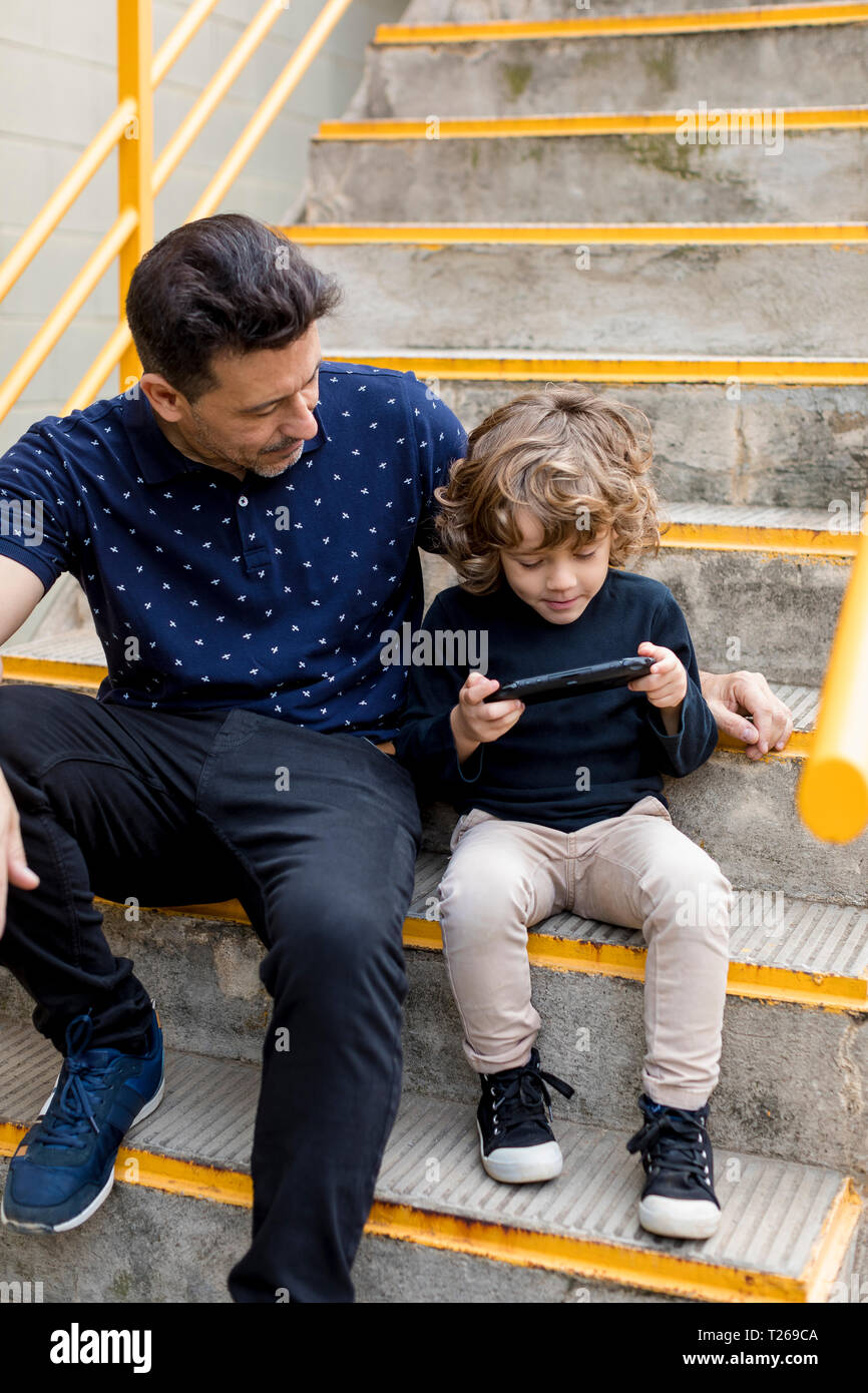 Father watching son playing with handheld game console Stock Photo