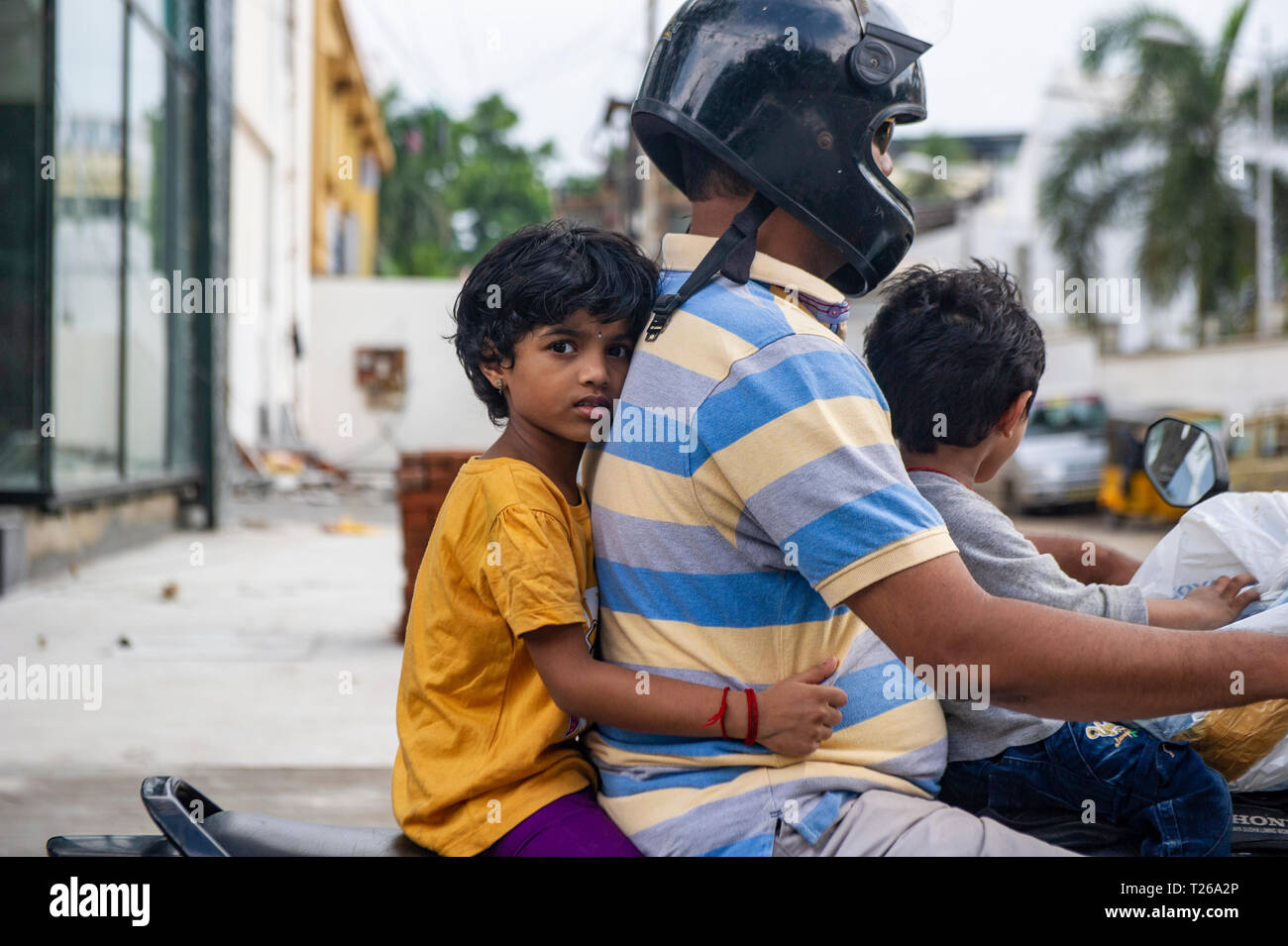 A father wears a crash helmet on his scooter with his two children in the hustle and bustle of downtown Chennai, India Stock Photo