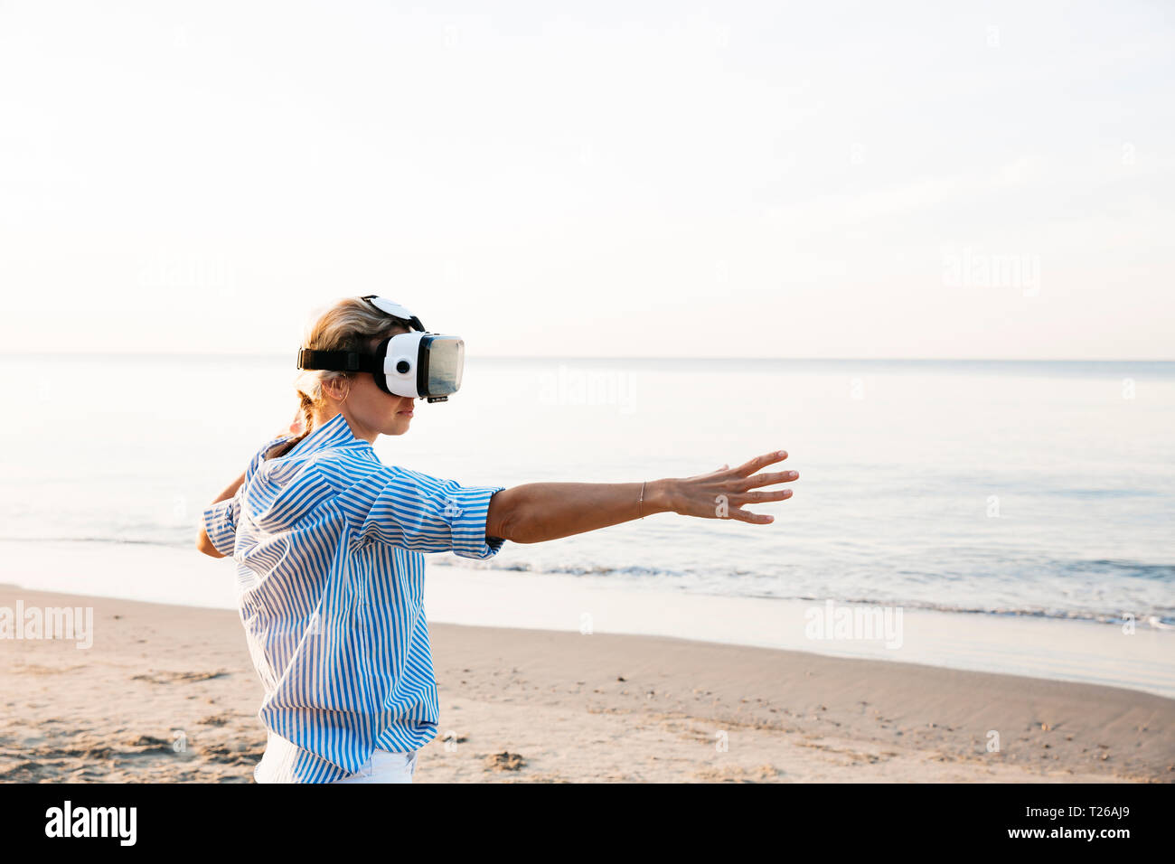 Blonde woman doing kind of yoga exercises on a beach in thailand with 3D virtual reality goggles Stock Photo