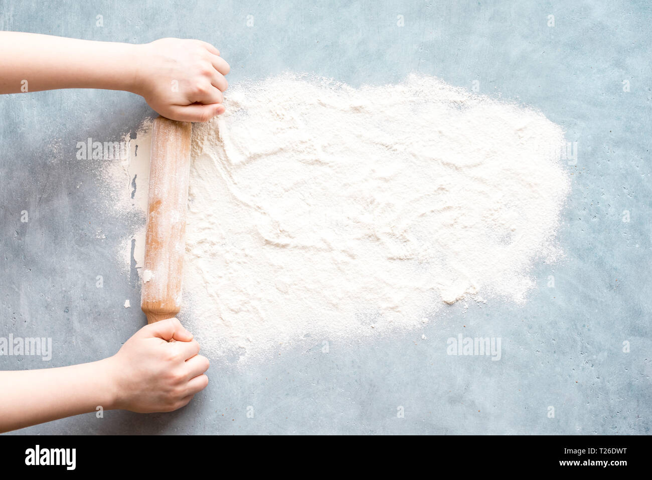 Flour and rolling pin in hands on blue background, top view, copy space. Homemade baking concept, space for text. Stock Photo