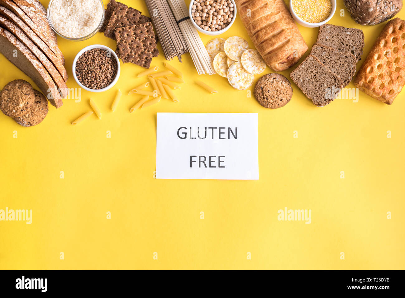 Gluten free food. Various gluten free pasta, bread, snacks and flour on yellow background, top view, copy space. Stock Photo