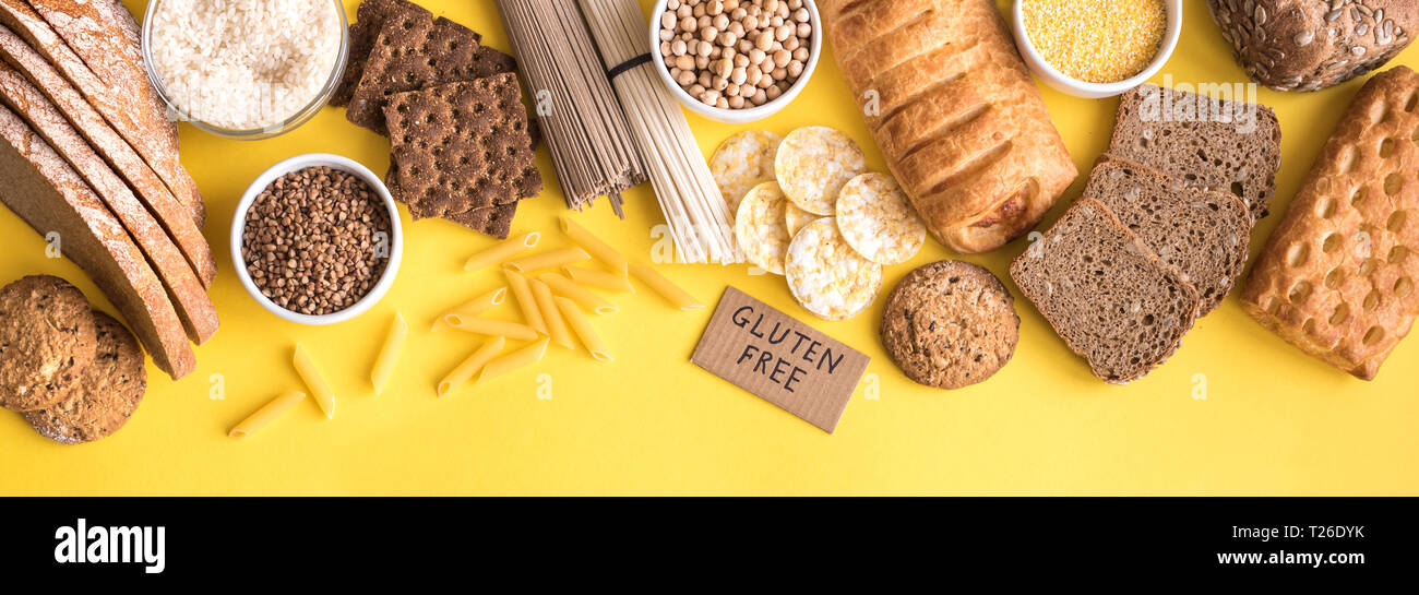 Gluten free food. Various gluten free pasta, bread, snacks and flour on yellow background, top view, banner. Stock Photo