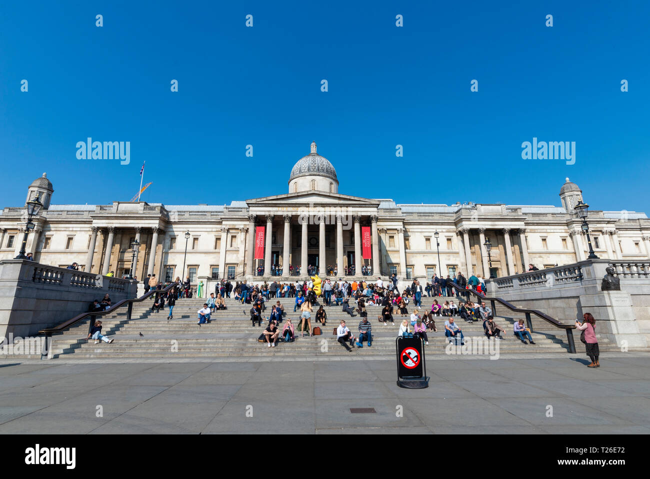 The National Gallery art museum and steps with tourists people, Trafalgar Square, London, UK. Sunny day with blue sky. Warm Stock Photo