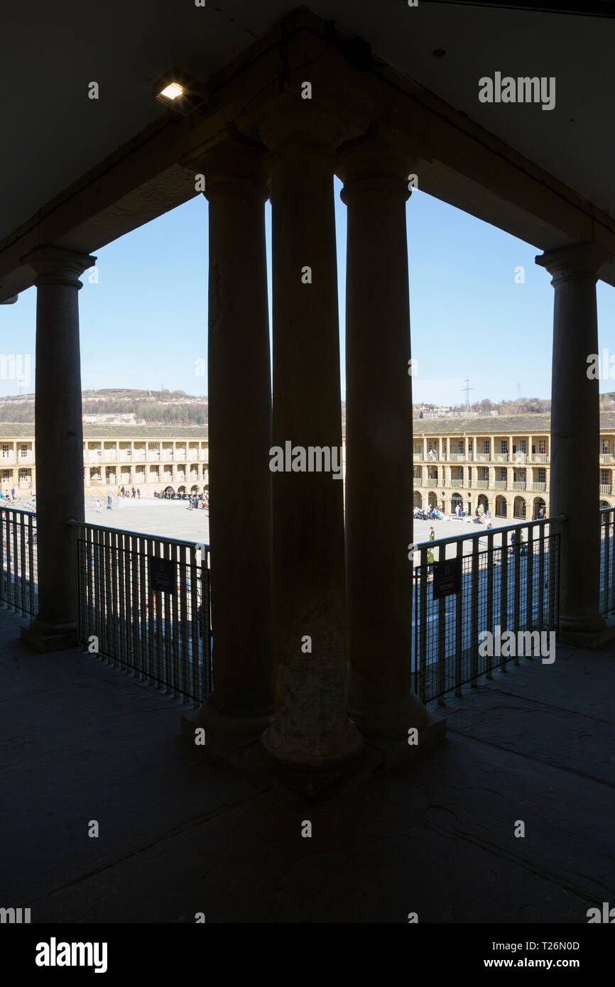 Elevated view through the columns of the upper colonnade of The Piece Hall with square quadrangle below. Sunny / sun & blue sky. Halifax, West  Yorkshire. England UK Stock Photo