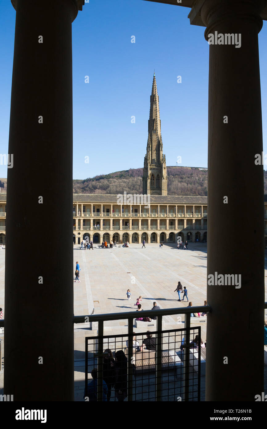 Elevated view through the columns of the upper colonnade of The Piece Hall with Square Chapel church spire behind in the background. Sunny / sun & blue sky. Halifax, West Yorkshire, UK. (106) Stock Photo