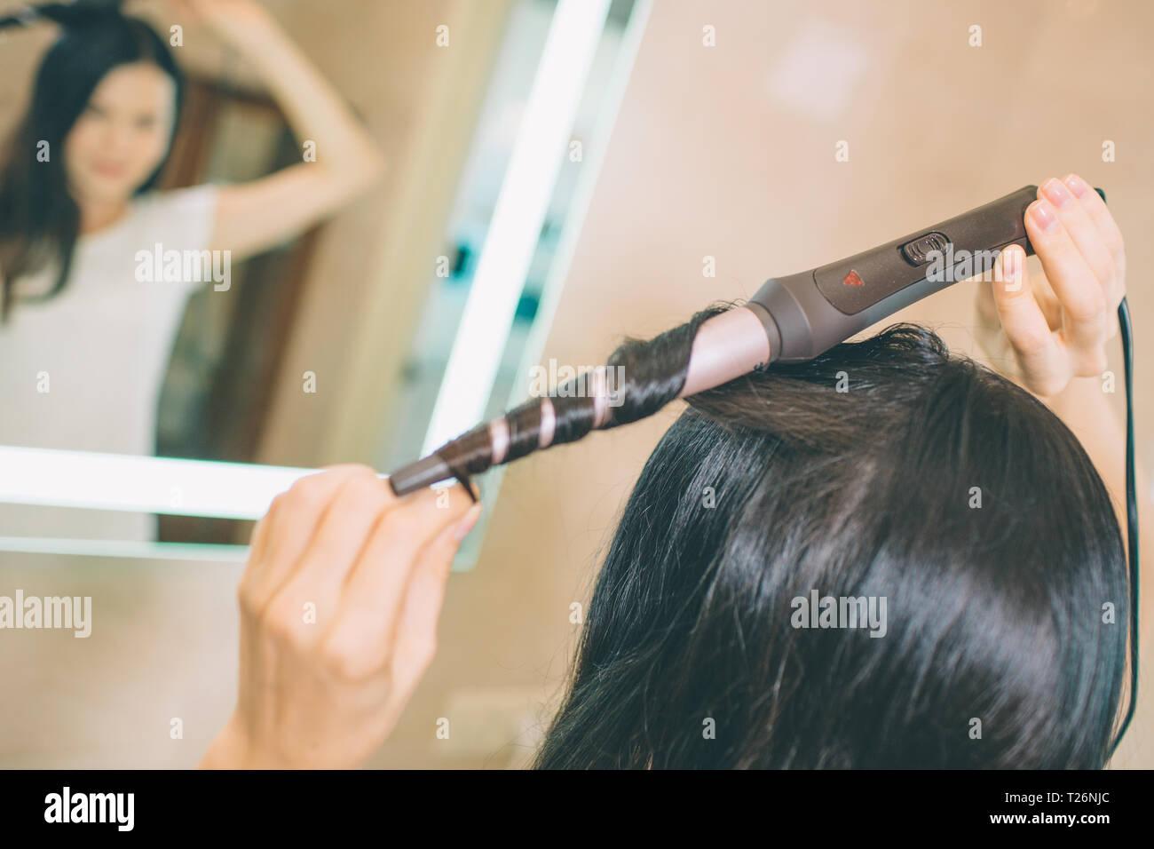 Close up of hair curling device Brunette uses it for making hair style. She  stands in front of mirror in bathroom. It is lightened with white light. S  Stock Photo - Alamy