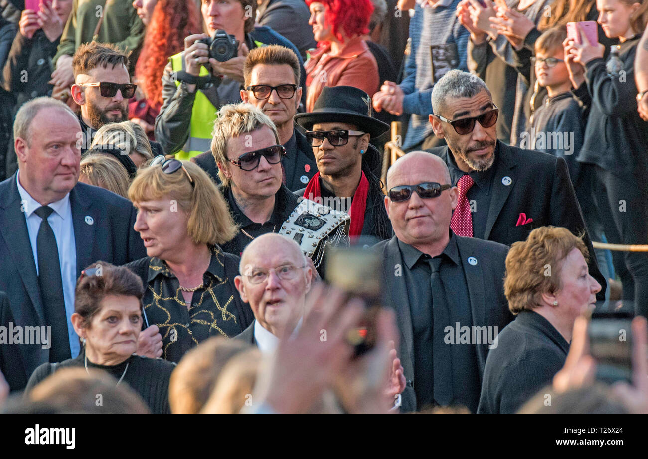 Essex, UK. 30th March 2019. The  funeral of Prodigy singer Keith Flint at St Marys Church in Bocking,  Essex today. Mourners leave the service and band members Liam Howlett, Maxim (Keith Palmer) and Leeroy Thornhill can be seen following Keith’s father Clive Flint out of the front gates of the church. Credit: Phil Rees/Alamy Live News Stock Photo