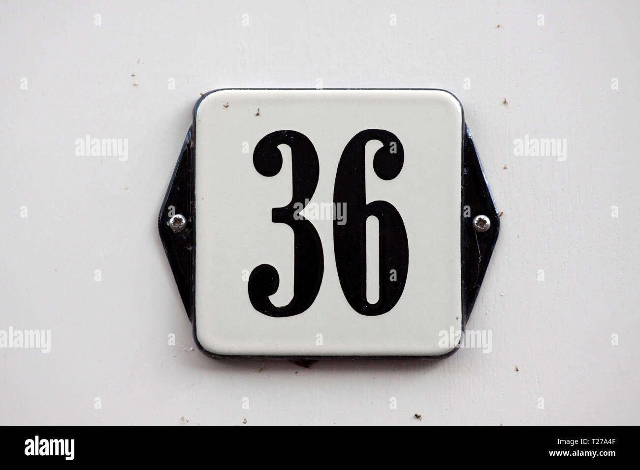 White with black enameled house number plate 36 screwed onto a white wall Stock Photo