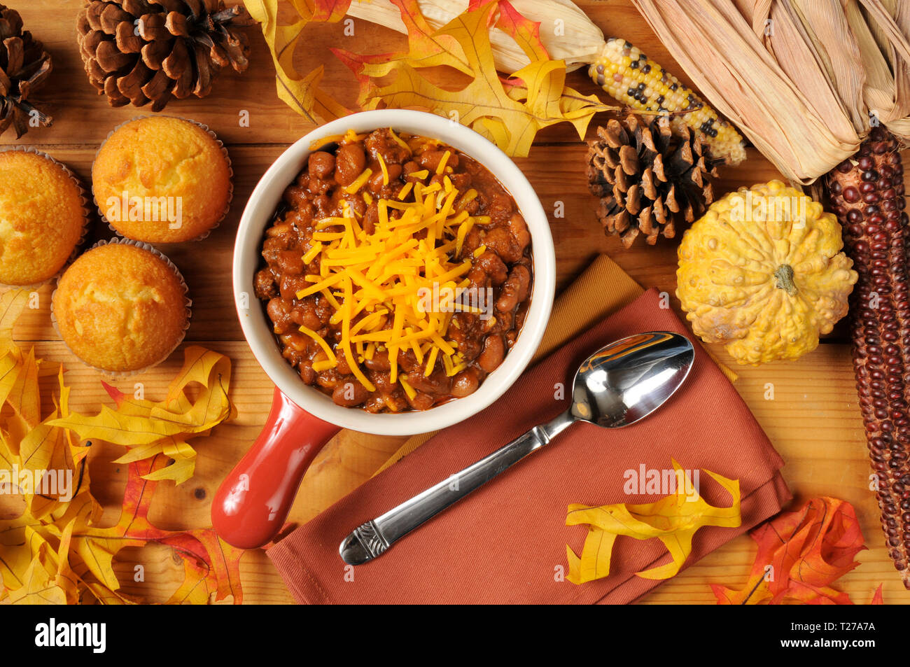 A stoneware crock of chili con carne with cornbread muffins and cheddar
