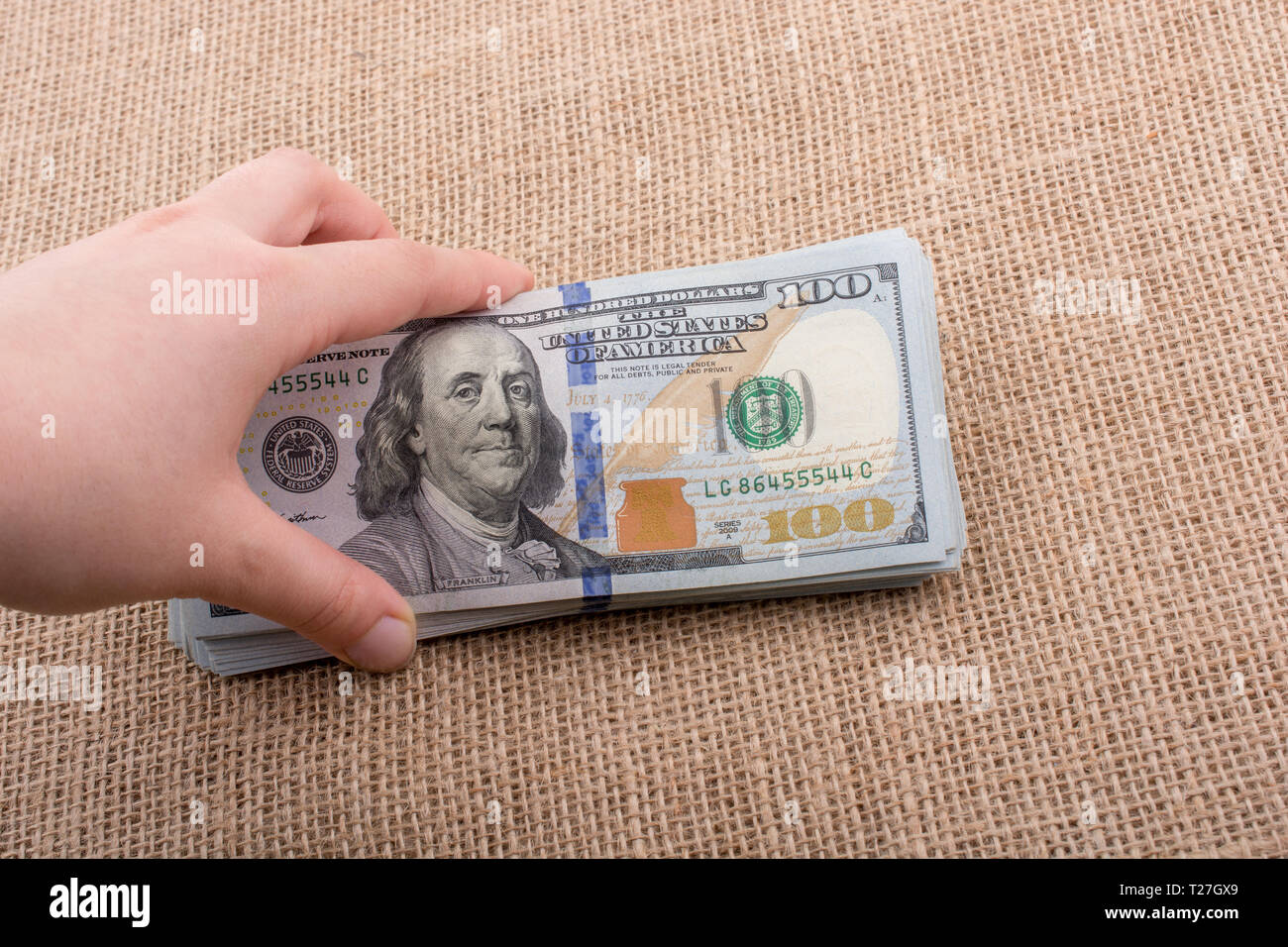 Hand holding banknote bundle of US dollar on a linen canvas background ...