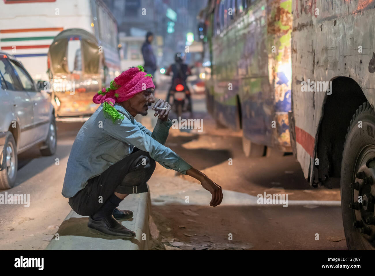 man in pink turban smokes cigarette  while sitting in the middle of street, Dhaka, Bangladesh Stock Photo