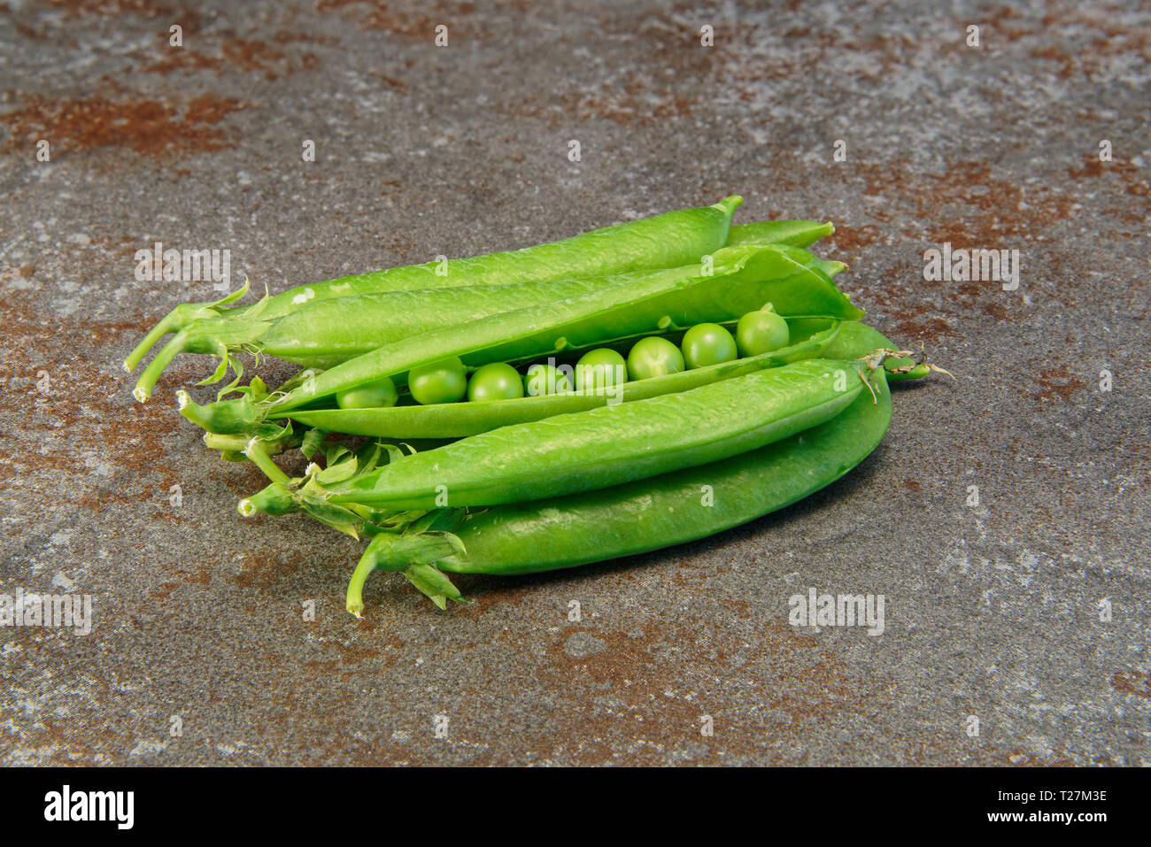 A pile of fresh green peas, one pod opened, placed on a kitchen worktop tile. Stock Photo