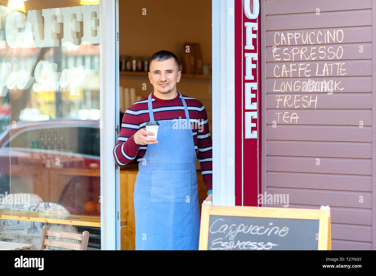 Portrait of small business coffee shop owner smiling and standing in front of shop serving a