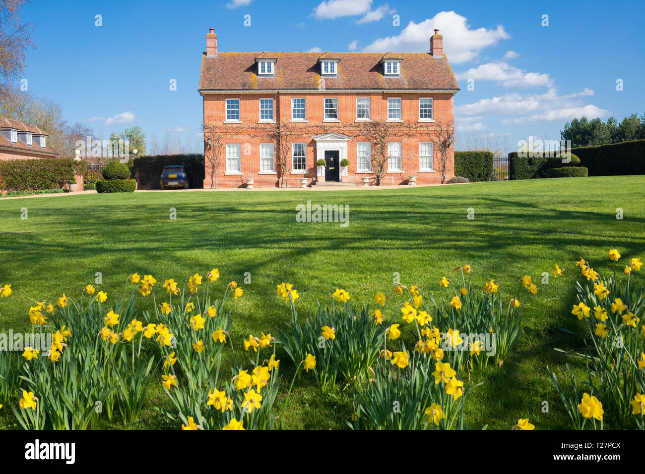 Elegant English Country Manor mansion house Grade 2 listed Victorian period property in red brick. Front view with large garden, green lawn and daffod Stock Photo