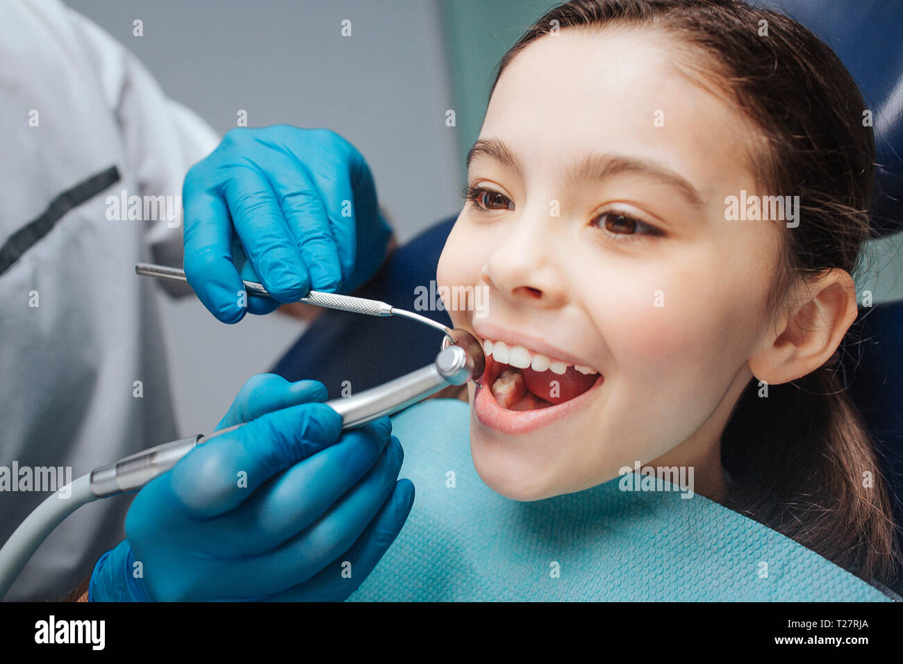 Happy girl sit in dentist chair. She keep mouth opened. Dentist use