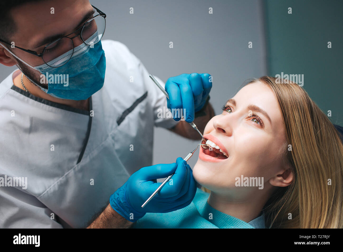 Close up of dentist checking client's teeth with special tools. Young woman sit in chair in room