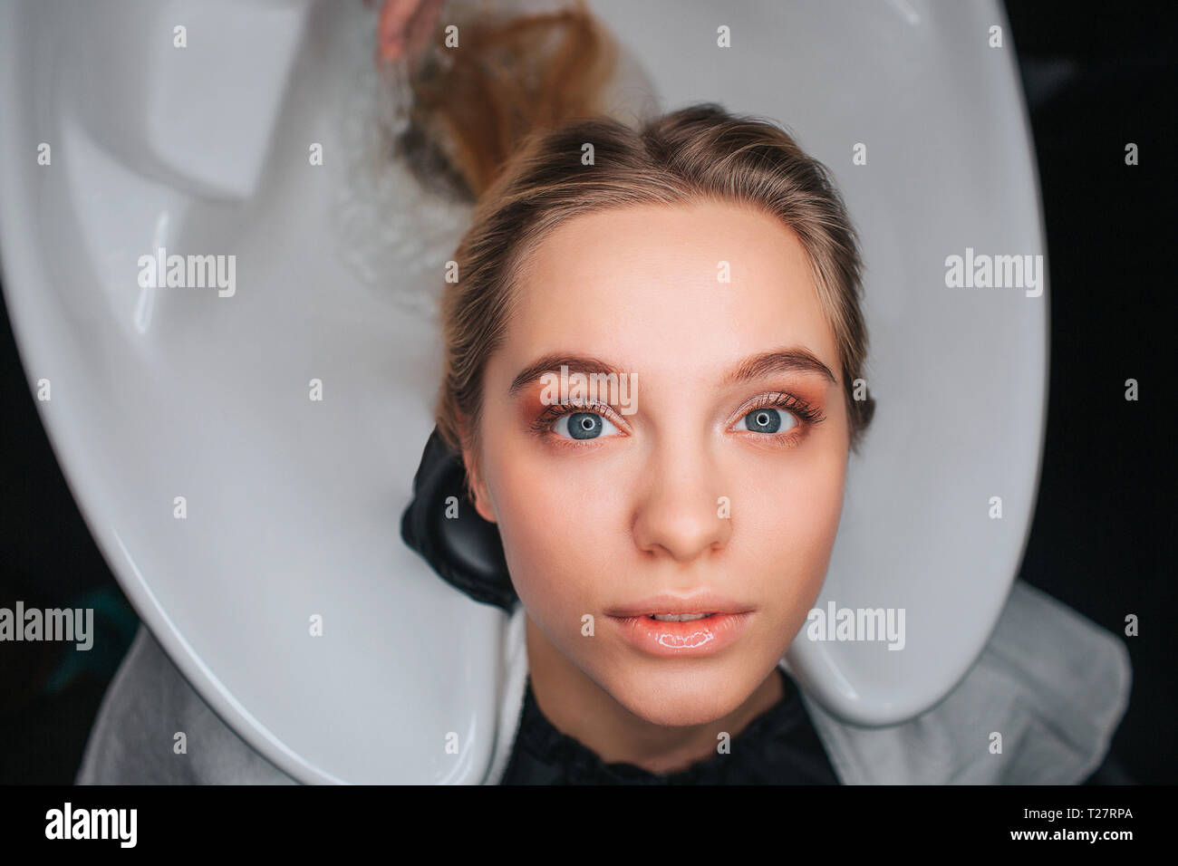 Portrait of blonde beautiful young woman sitting on white hair wash sink and waiting for a hairdresser. Washing hair in beauty salon Stock Photo