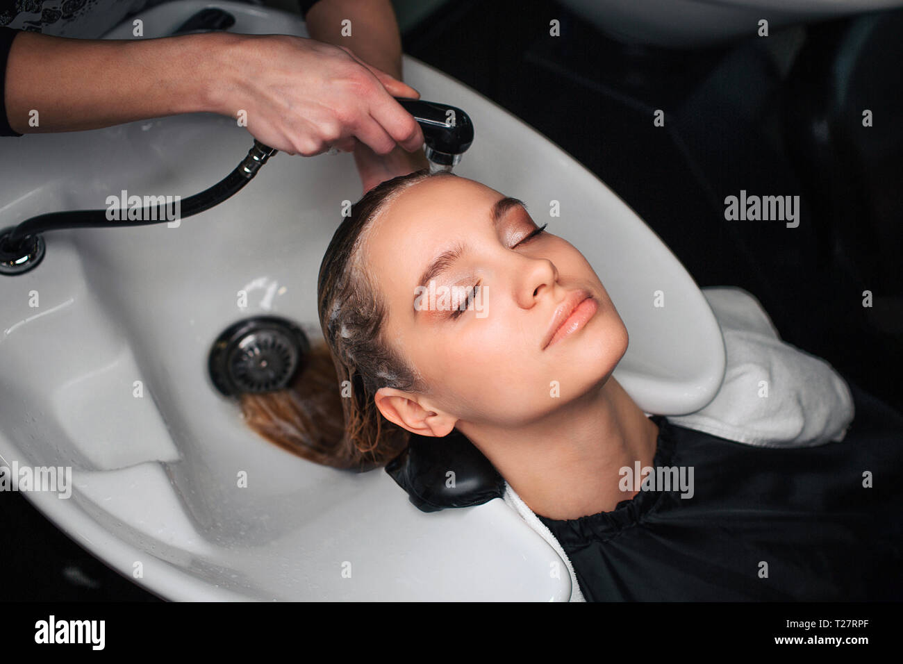 Side vew of attractive, beautiful woman with closed eyes sitting while hairdresser washing hair in beauty salon. Beauty and people concept Stock Photo