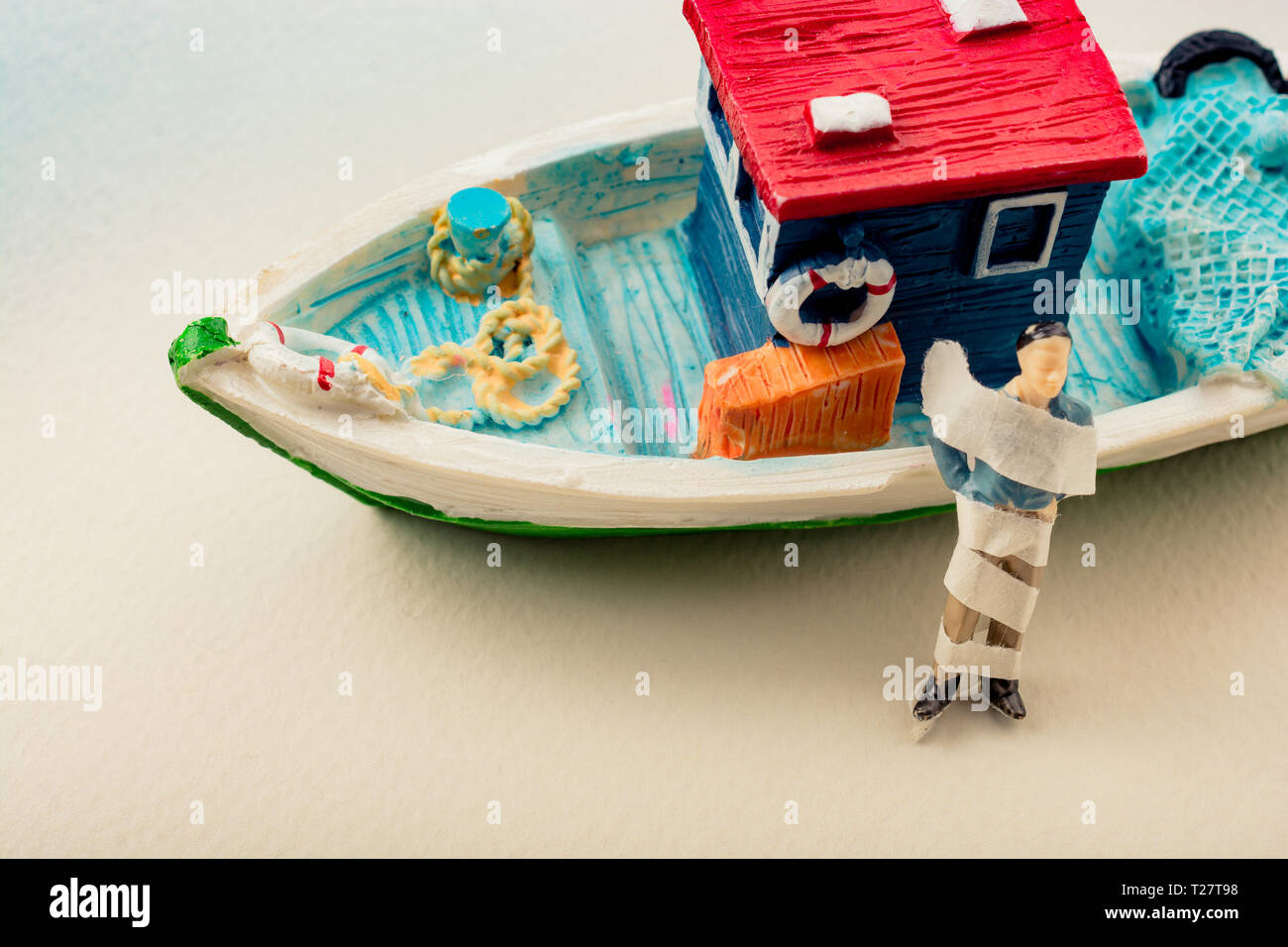 Tiny wrapped figurine of man model beside a model boat Stock Photo