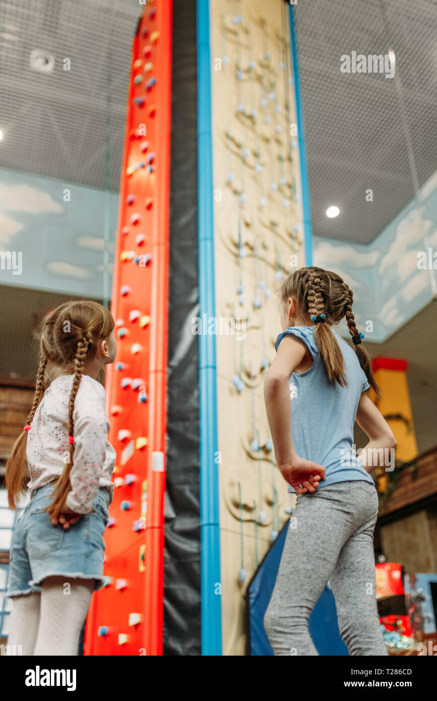 Two little girls looks on climbing wall, children game center. Excited childs having fun on playground indoors. Kids playing in amusement centre Stock Photo