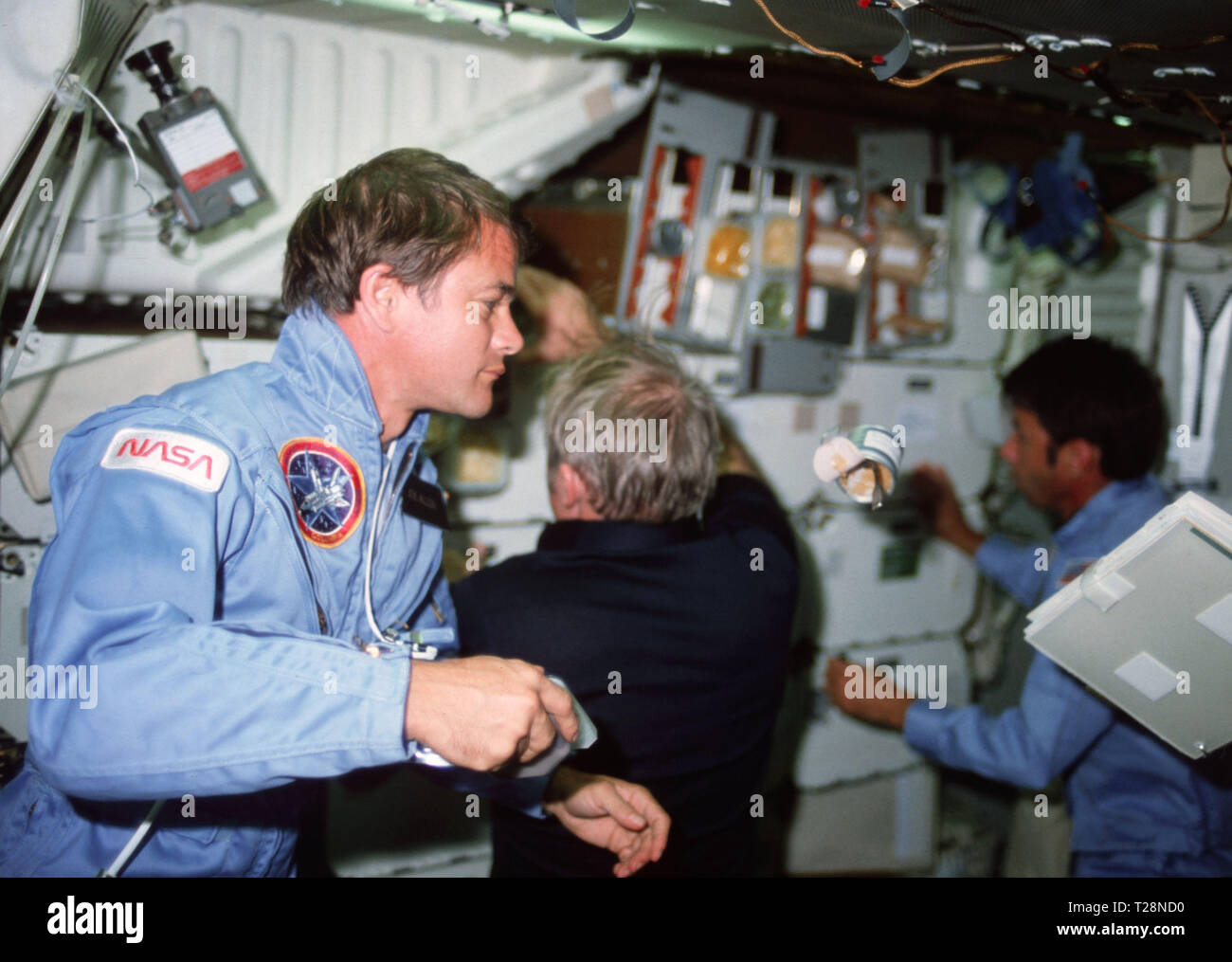 (11-16 Nov. 1982) --- Astronaut Joseph P. Allen, STS-5 mission specialist, watches a can of food and a notebook drift on the middeck as Vance C. Brand, commander, (left) and William B. Lenoir, mission specialist, (far left) work at forward middeck lockers. Stock Photo