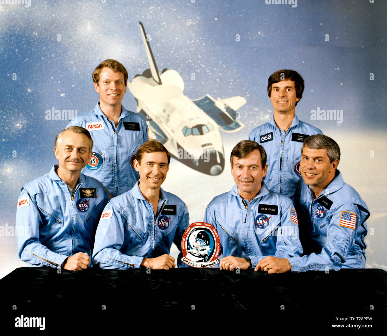 The four NASA astronauts are joined by a European and MIT scientist payload specialist and the Spacelab module and experiment array for STS-9. On the front row are Astronauts Owen K. Garriott, mission specialist; Brewster H. Shaw, Jr., pilot; John W. Young, commander; and Robert A. R. Parker, mission specialist. Byron K. Lichtenberg of the Massachusetts of Technology, left and Ulf Merbold of the Republic of West Germany and the European Space Agency stand in front of an orbital scene featuring the Columbia. Columbia was used for the first five Space Transportation System missions in 1981 and 1 Stock Photo