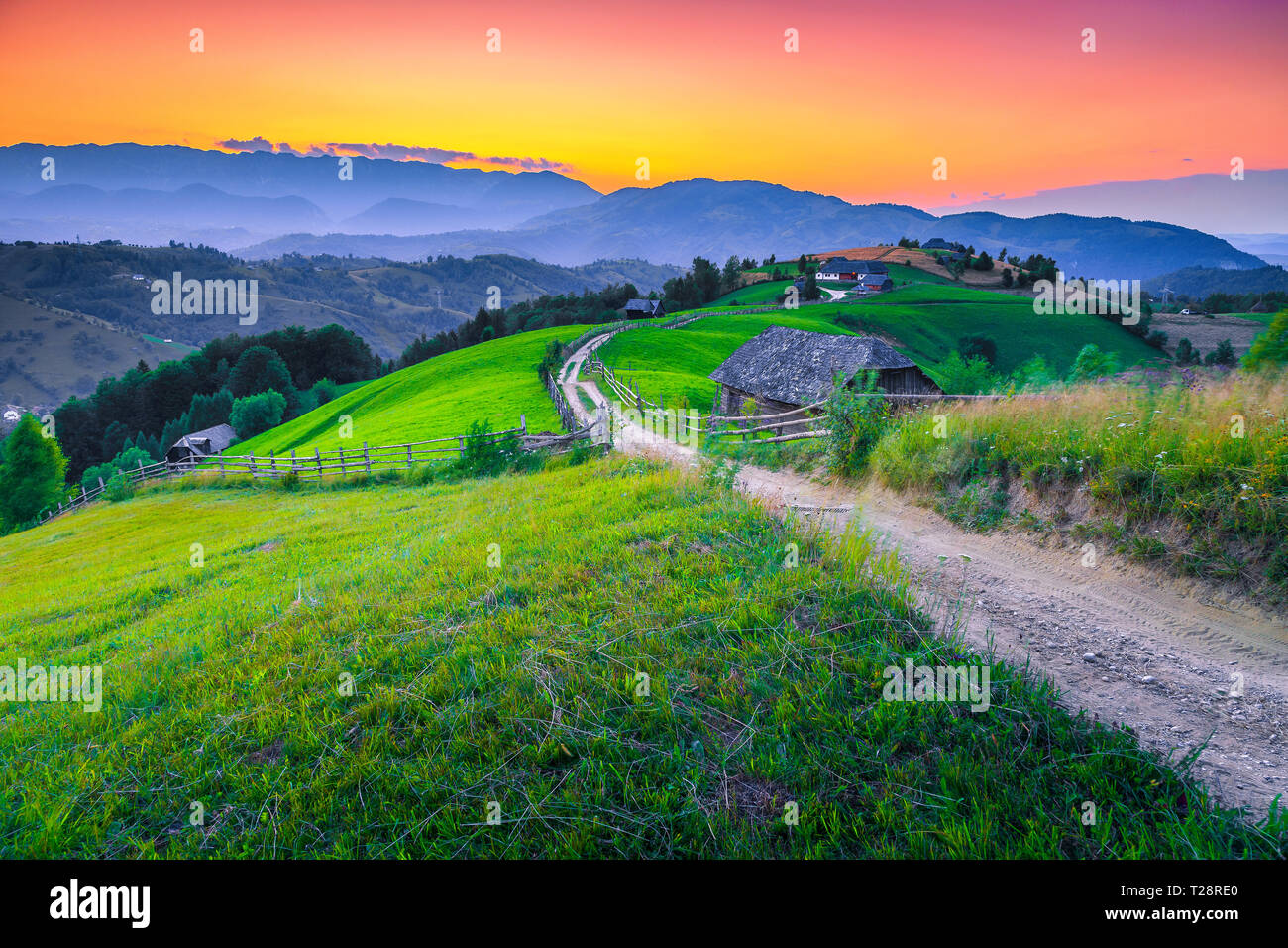 Fantastic travel destination, majestic summer rural landscape, green fields and wooden houses with gardens at sunset, Bran, Transylvania, Romania, Eur Stock Photo