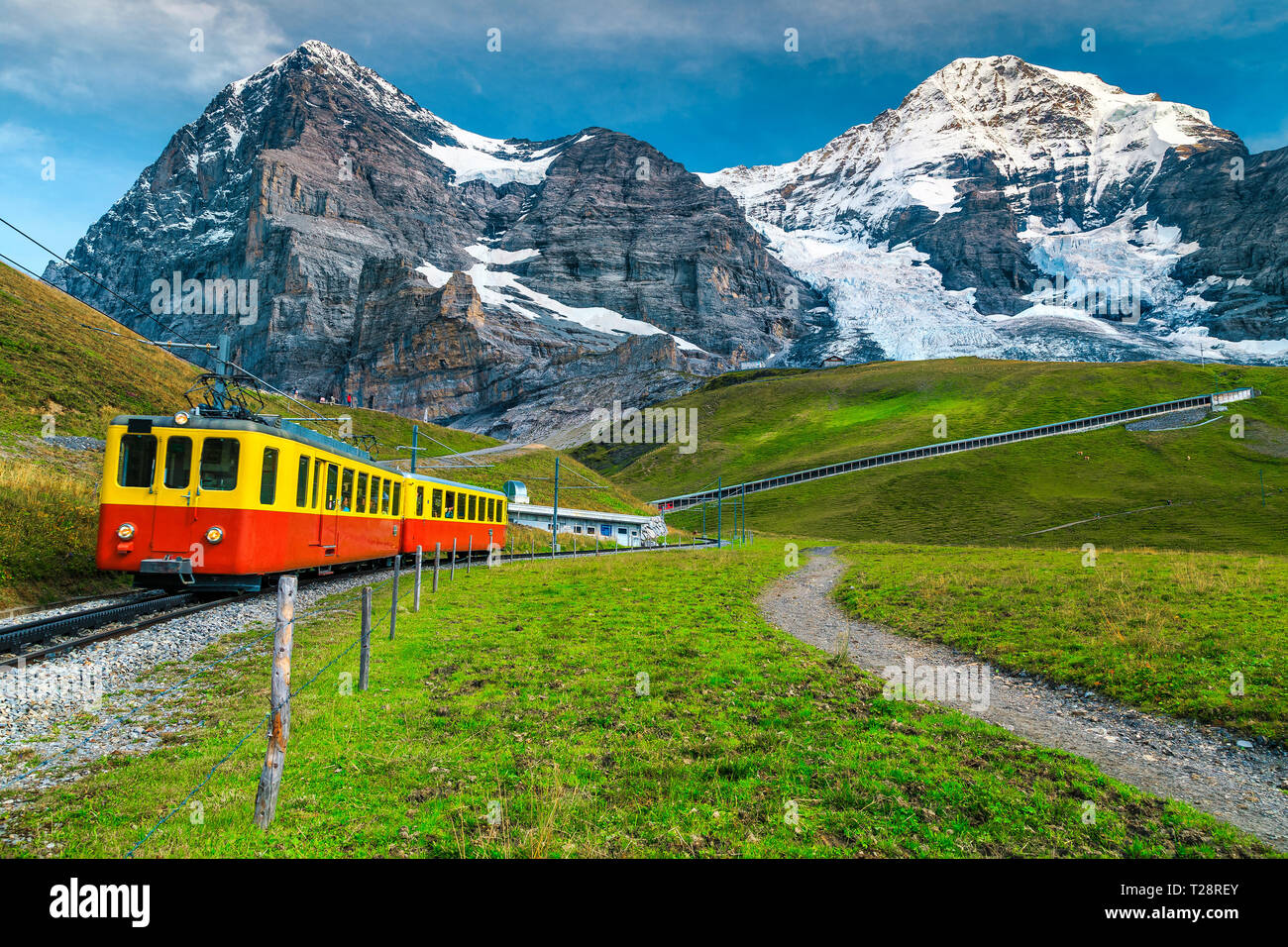 Gorgeous summer travel experience, popular electric red tourist train with high snowy Swiss mountains in background, near Kleine Scheidegg station, Be Stock Photo
