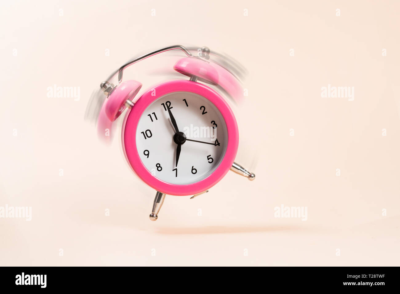 Pink bouncing ringing alarm clock on a beige background. Motion blur ...