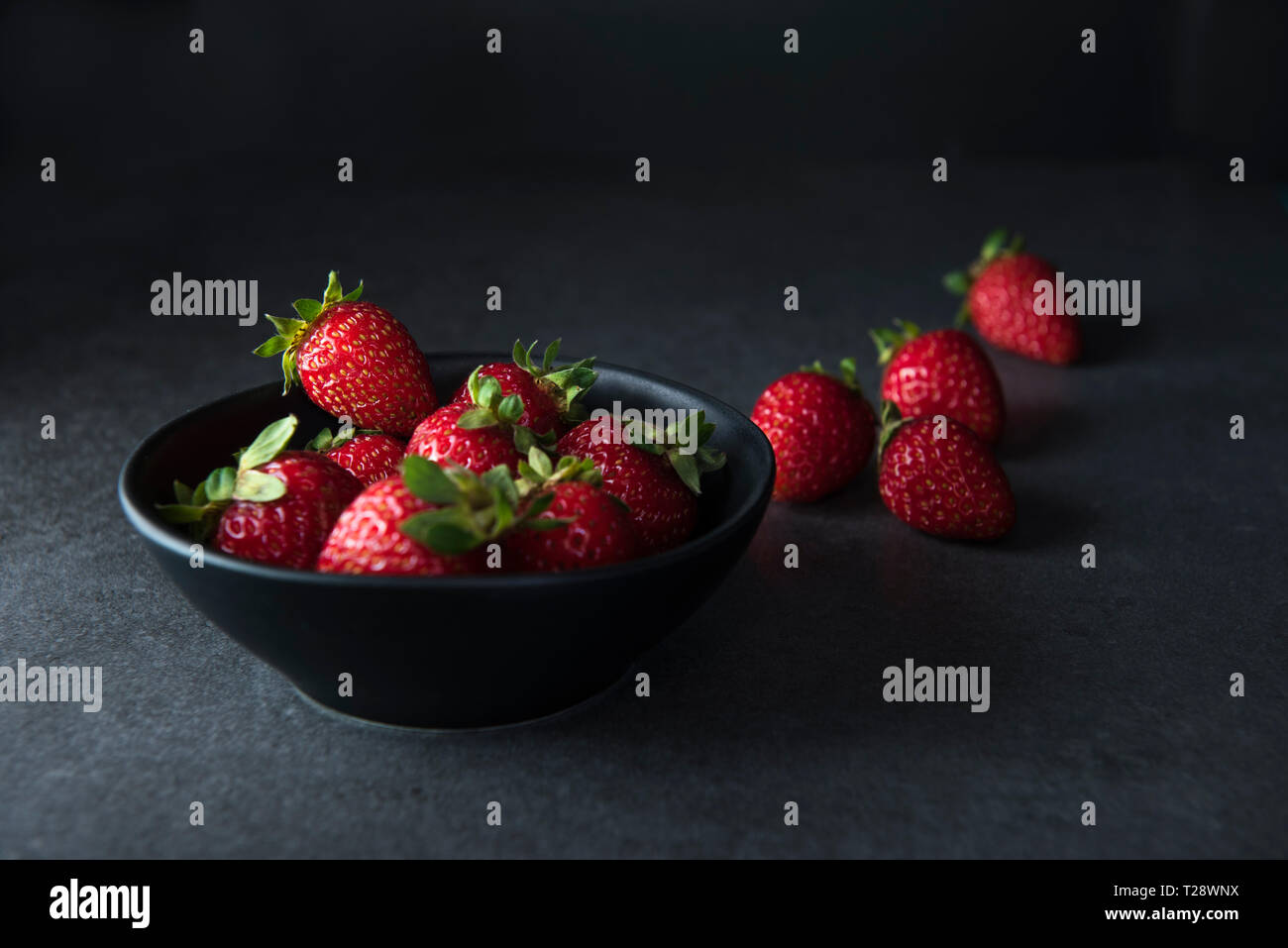 Strawberries in dark bowl on dark background with copy space, low key image Stock Photo