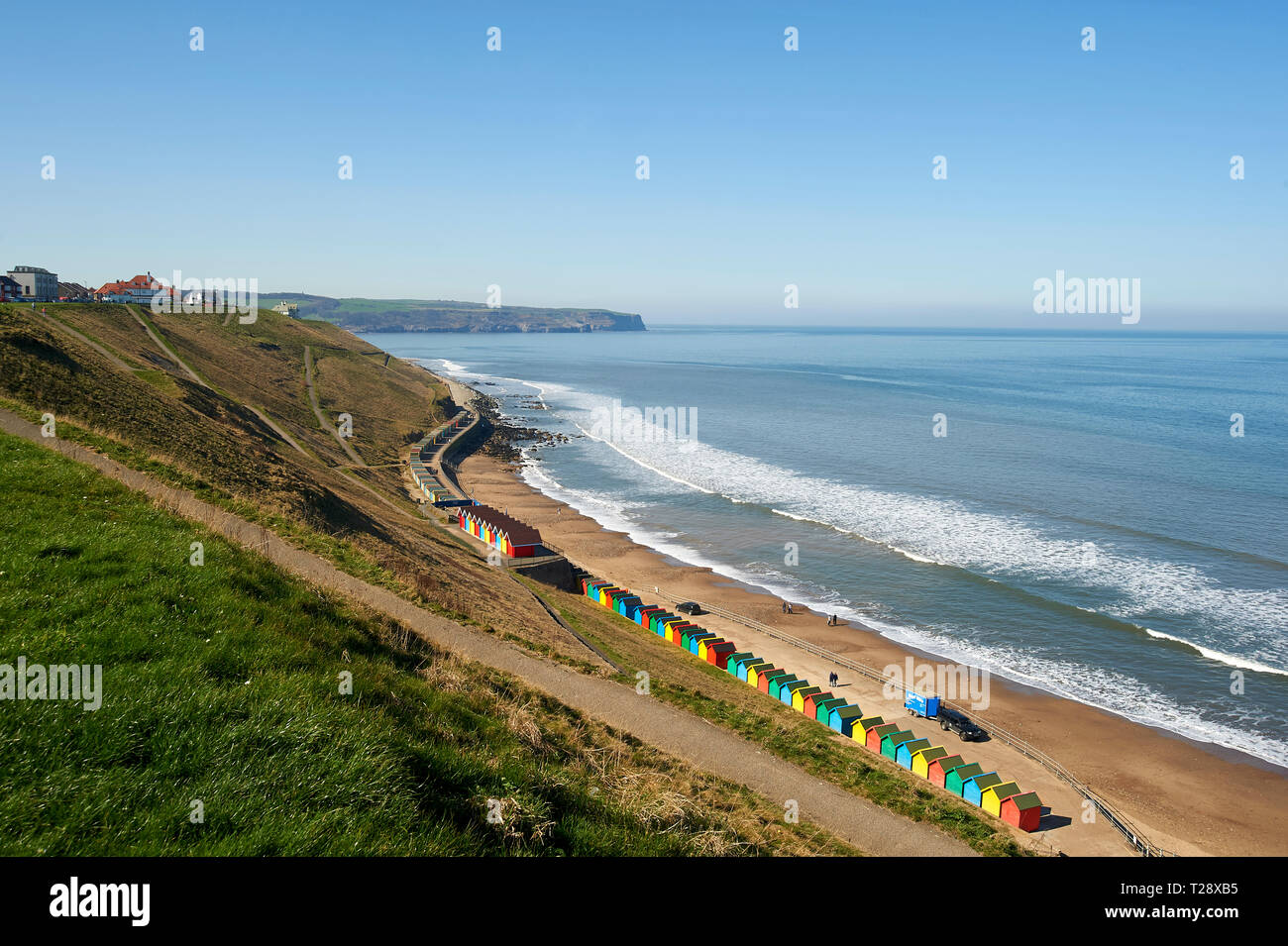 People walking past the Colourful beach huts, west cliff, Whitby, North Yorkshire Coast, England, UK, GB. Stock Photo