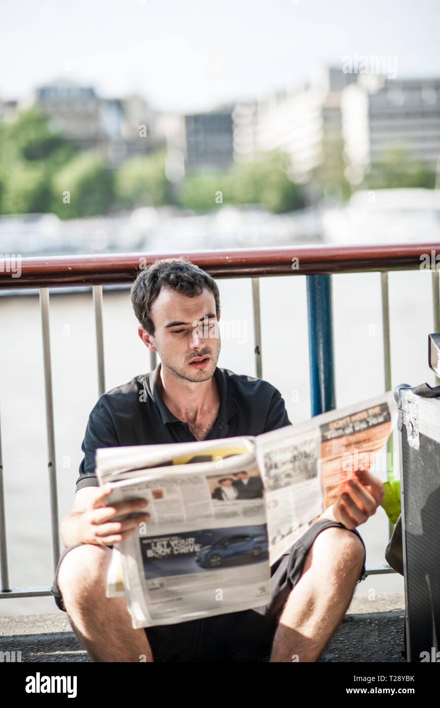 A man reads a newspaper during the summer beside the River Thames in London. UK. Stock Photo