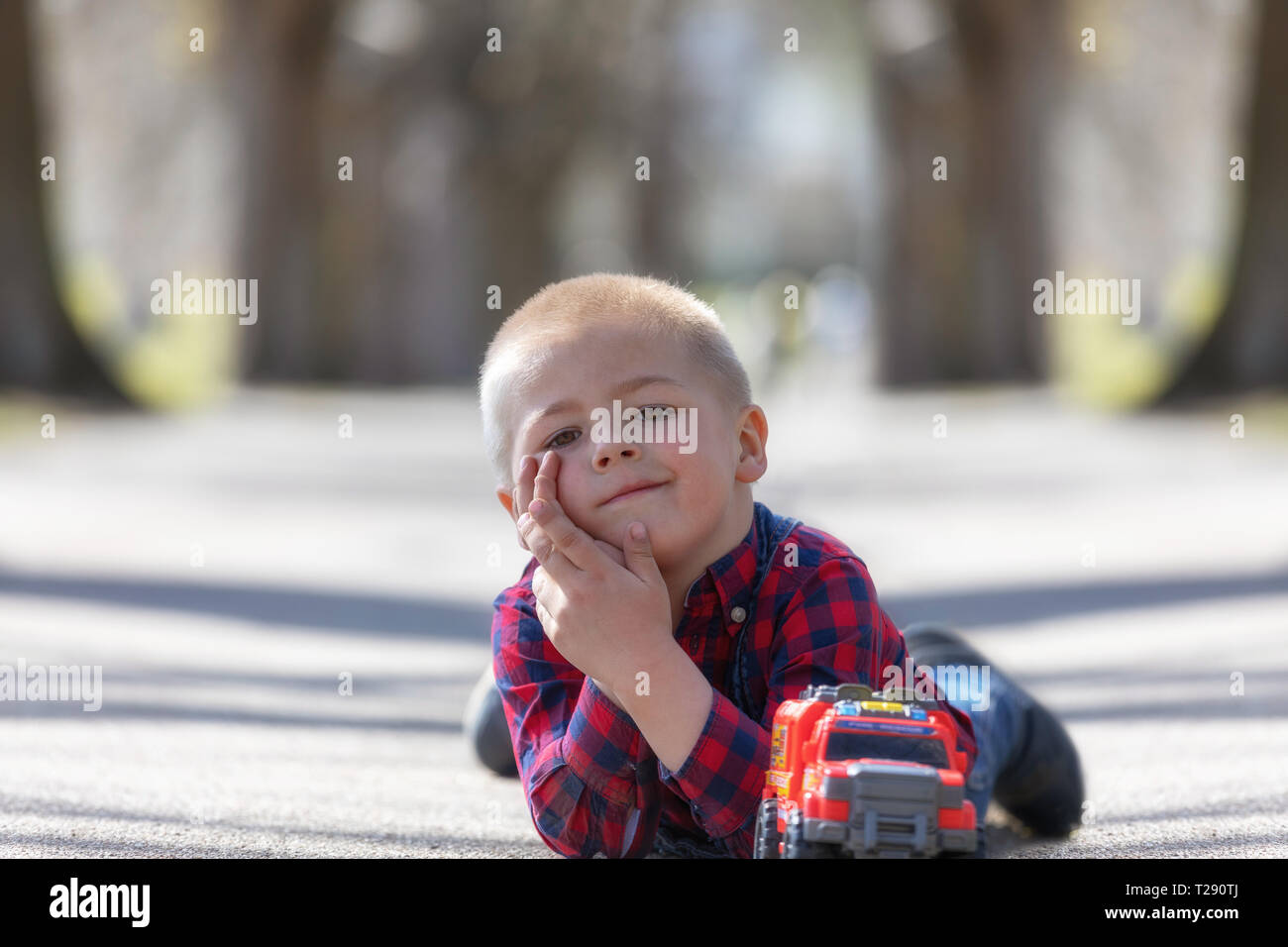 Cute little child, blonde toddler boy playing outdoors lying at street Stock Photo