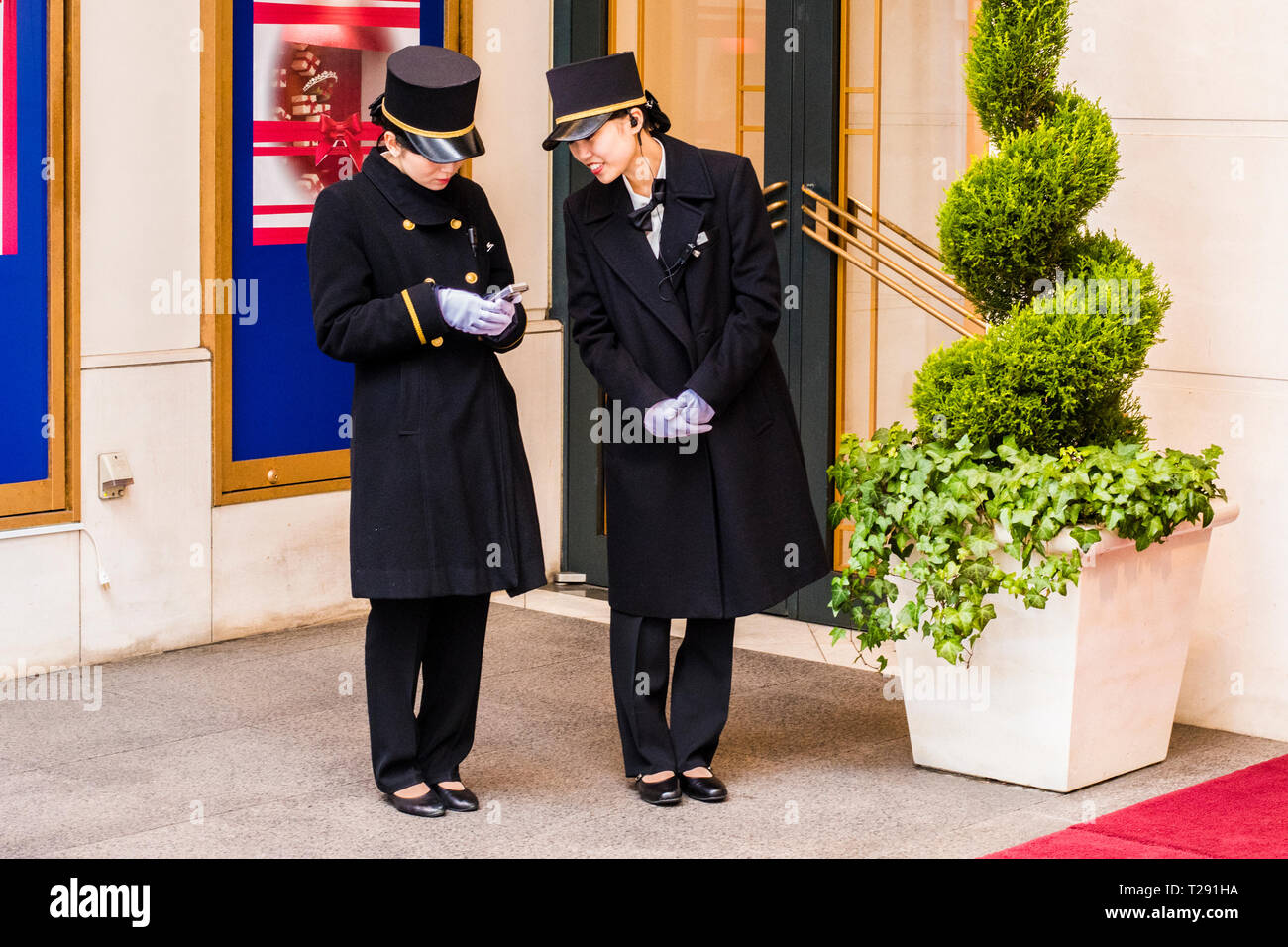 Two female hotel porters, standing outside hotel, looking at smartphone, Omotesando Area, Tokyo, Japan Stock Photo