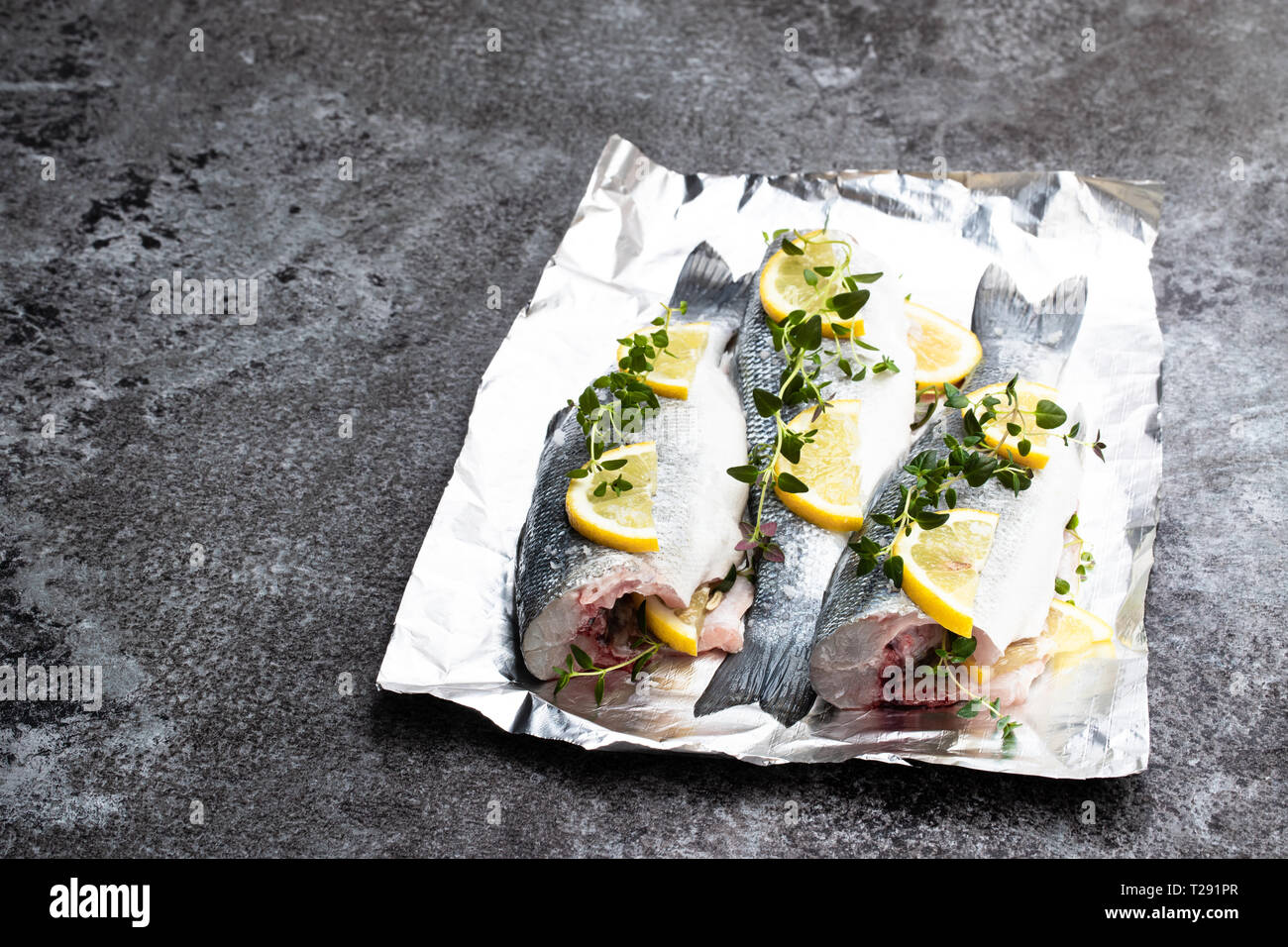 Fresh whole sea bass fish with lemon and herbs on foil on gray stone table Stock Photo Alamy